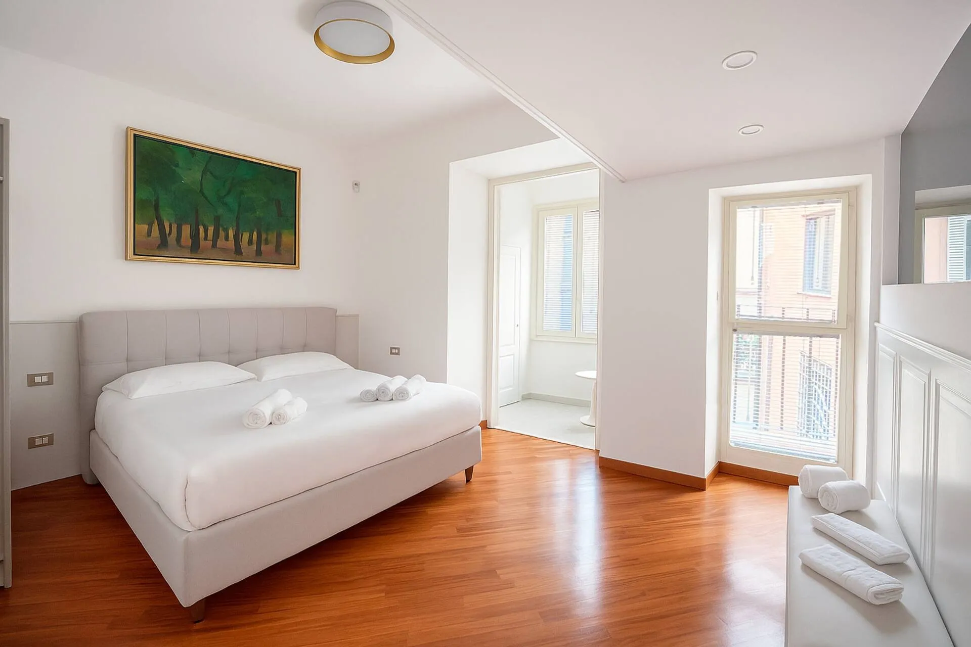 Camera con letto matrimoniale bianco, parquet e due porte finestre