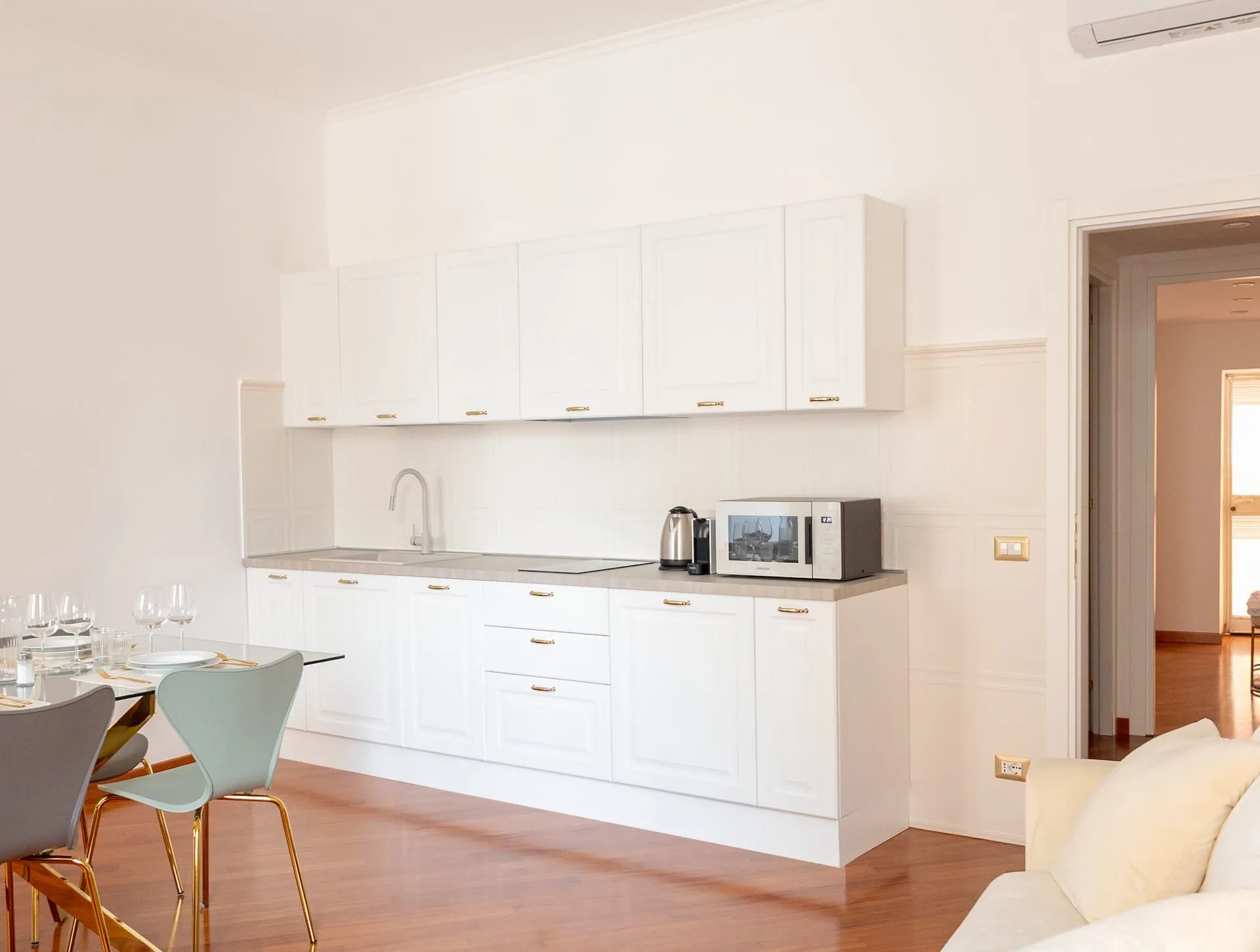 Cucina bianca con microonde e bollitore, sedie azzurre in primo piano