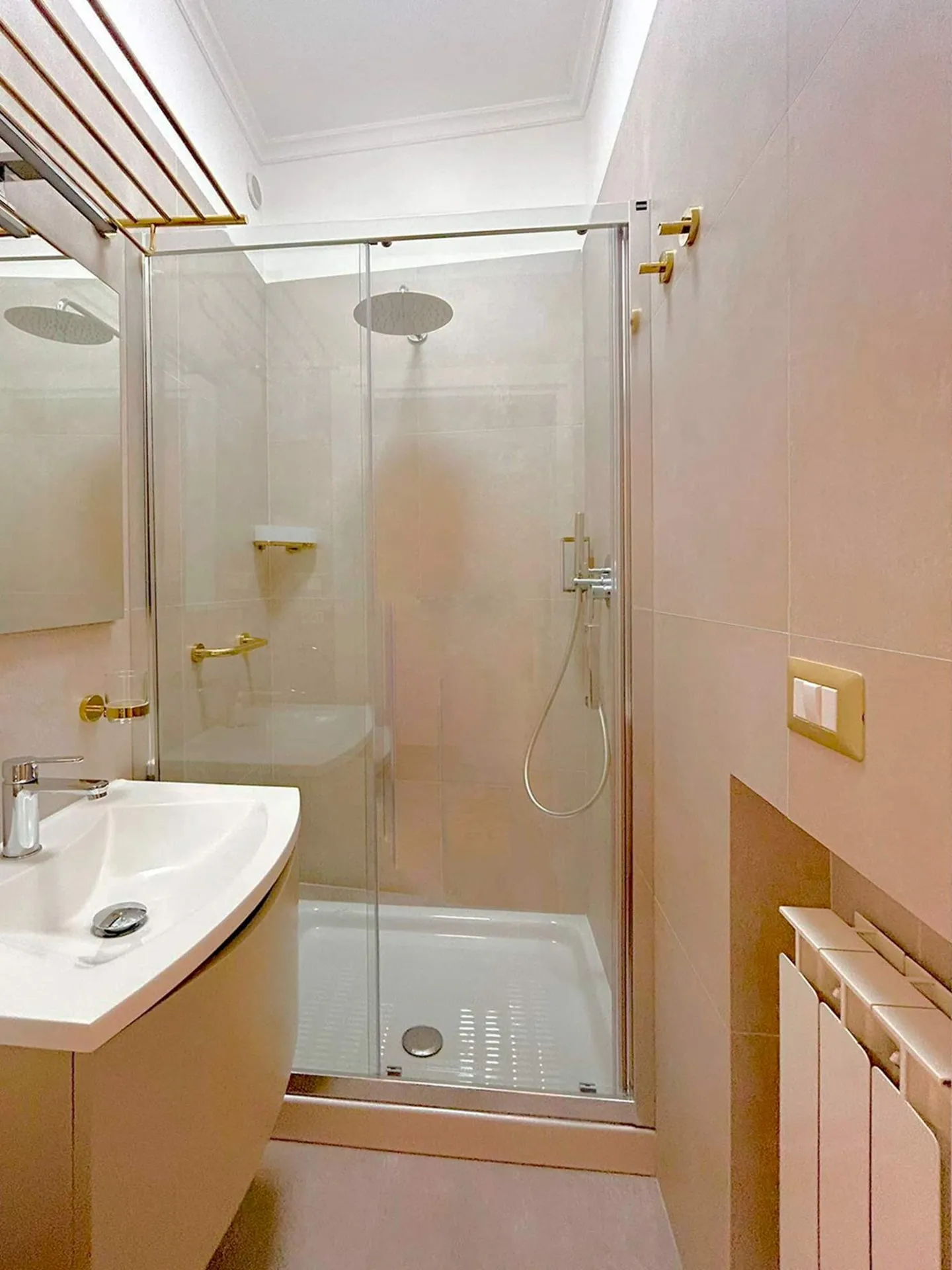 Bagno chiaro con doccia in vetro e rubinetteria dorata