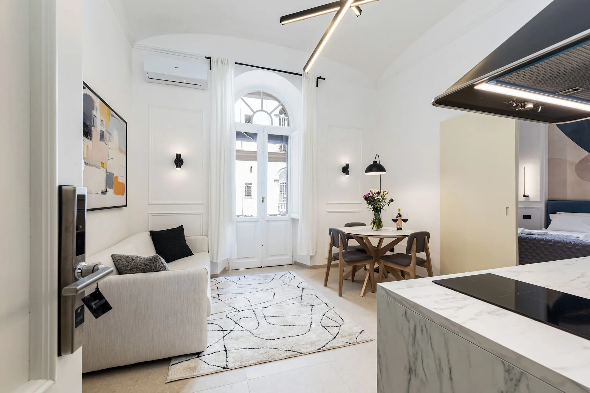 Soggiorno bianco con divano, tappeto disegnato e tavolo rotondo davanti alla porta finestra ad arco