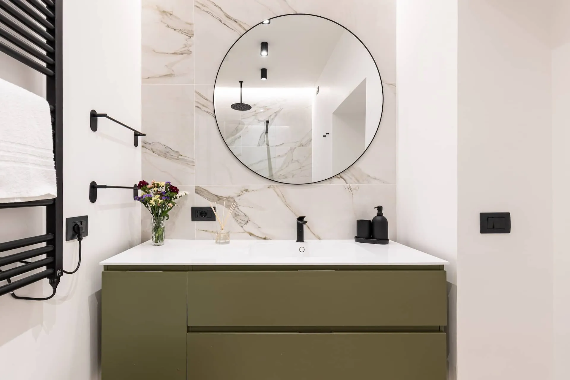 Bagno con mobile verde scuro, specchio rotondo e piastrelle effetto marmo