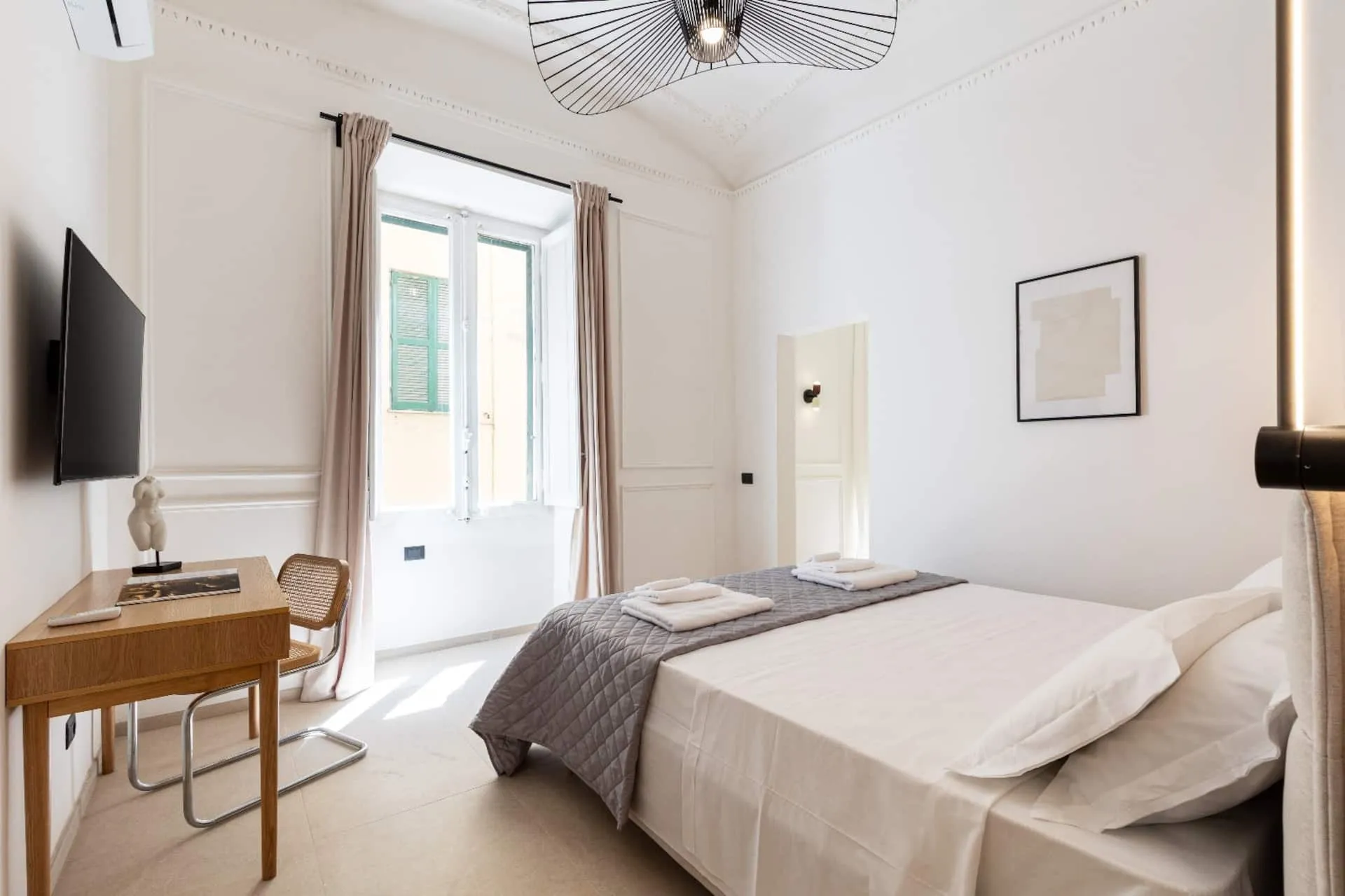 Camera vista dalla finestra: scrivania, letto e lampadario a raggiera