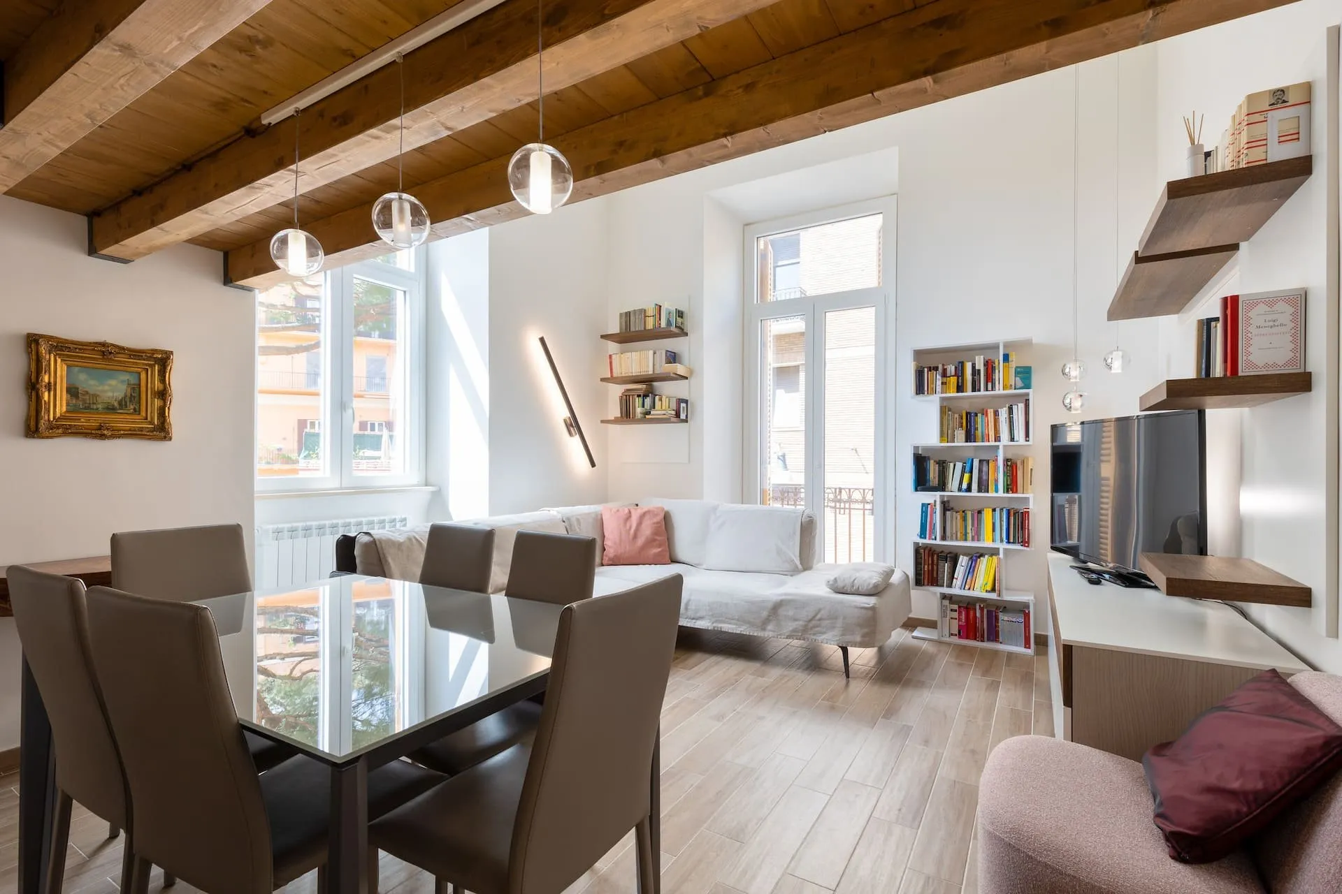 Soggiorno con soffitto a travi di legno, tavolo di vetro con sei sedie, divano bianco e libreria