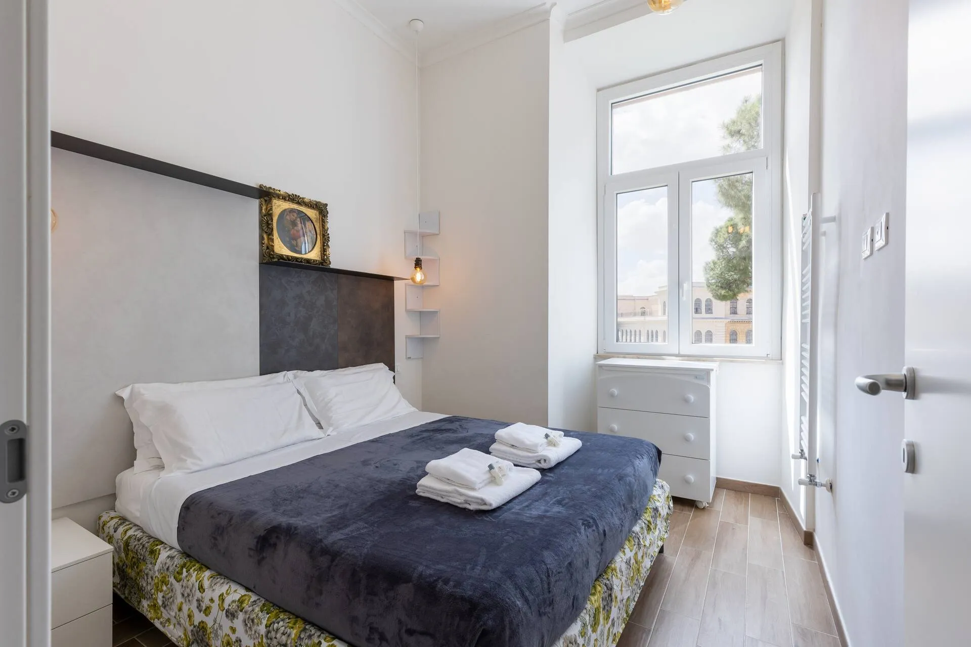 Camera con letto matrimoniale e coperta blu, finestra con vista sugli alberi