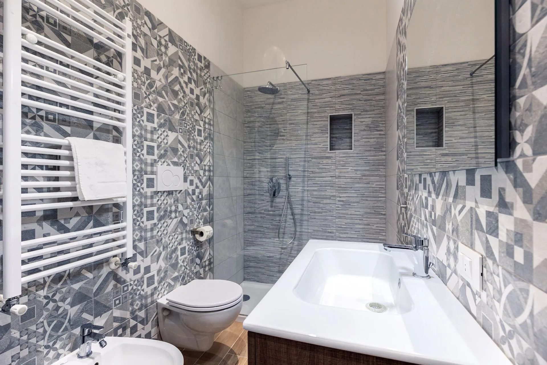 Bagno con piastrelle a motivi grigi, lavabo bianco e doccia