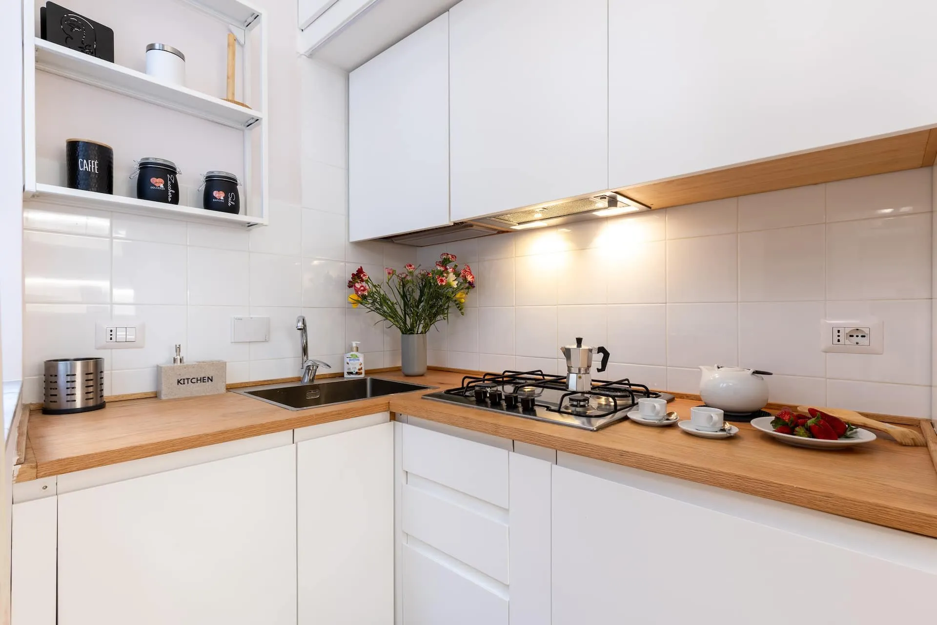 Cucina bianca ad angolo con piano di legno e fornelli a gas