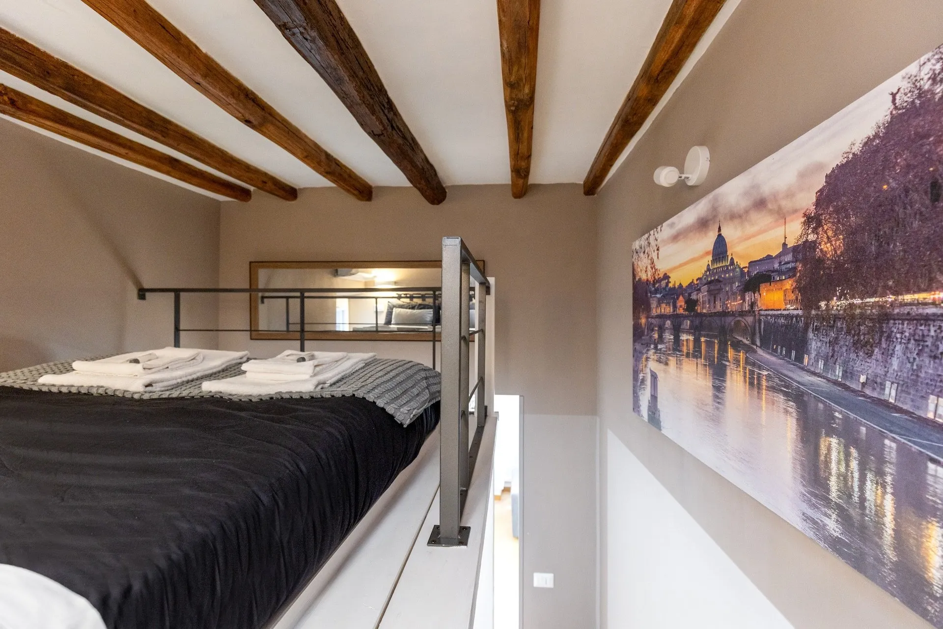 Letto sul soppalco sotto le travi, con una grande foto di Roma alla parete