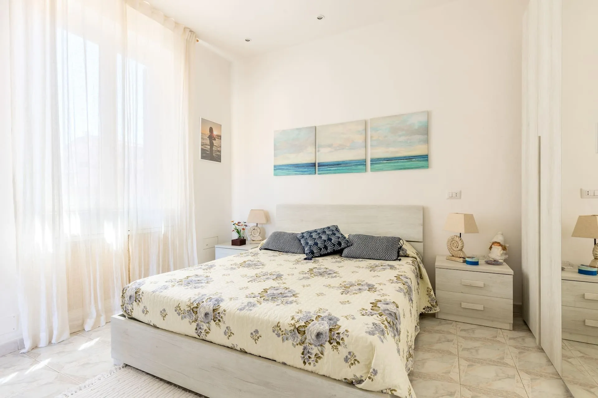 Camera con letto matrimoniale, copriletto a fiori e quadro del mare