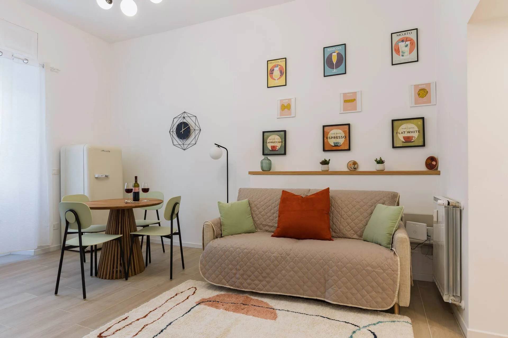 Soggiorno con divano beige e cuscini arancio, tavolo rotondo e quadretti colorati alla parete