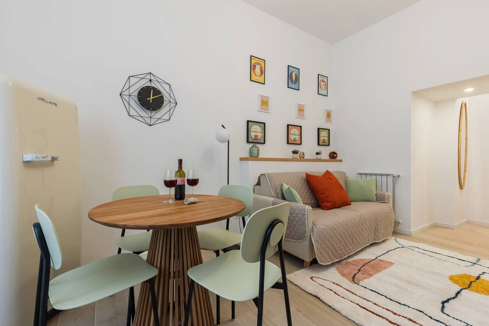 Tavolo rotondo con sedie verde acqua, orologio e divano beige sullo sfondo