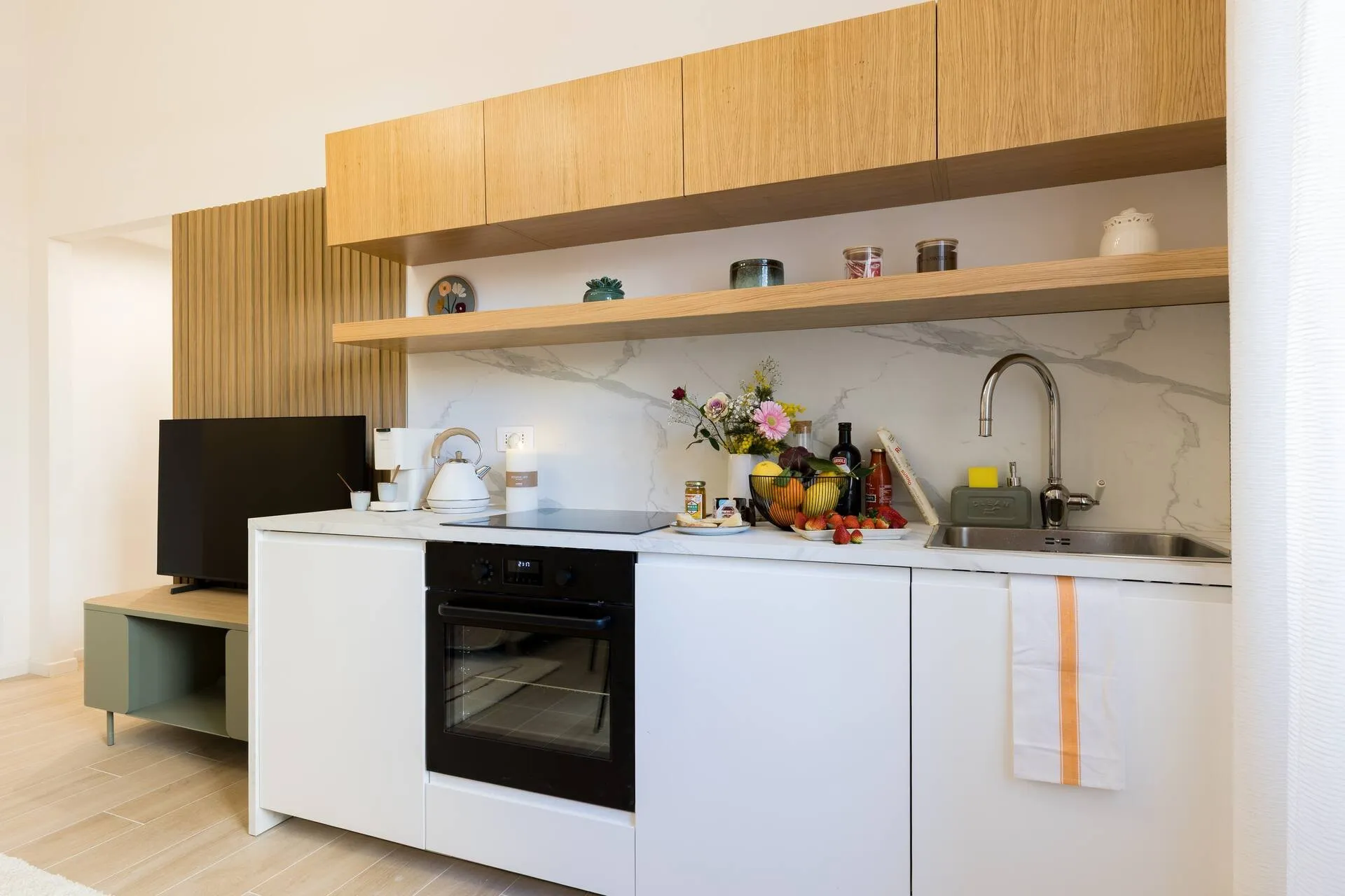 Cucina bianca con pensili e mensole di legno chiaro, forno e piano in marmo