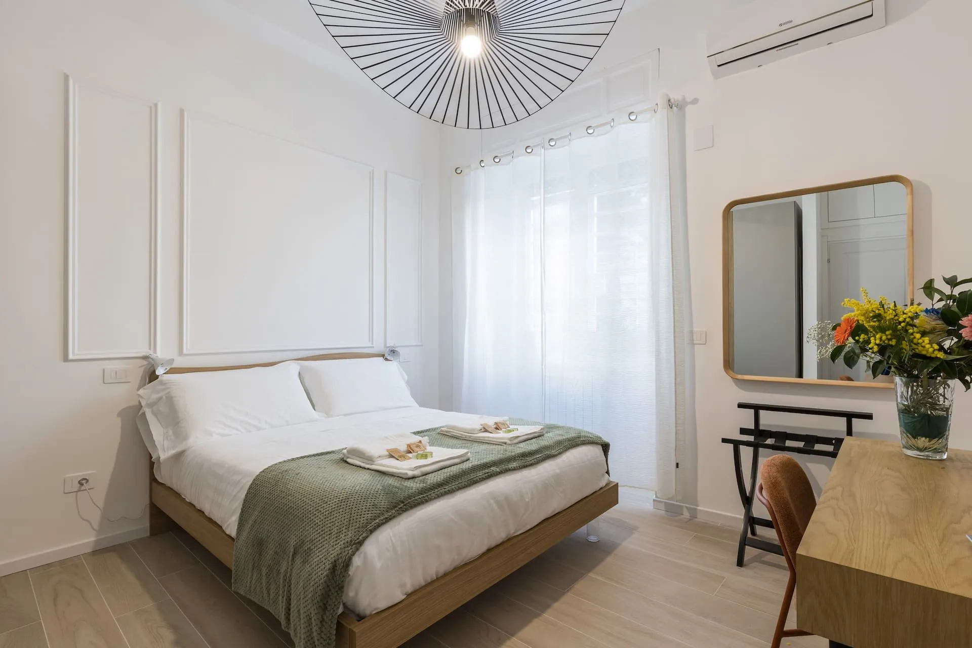 Camera con letto matrimoniale, coperta verde, specchio e fiori sulla scrivania