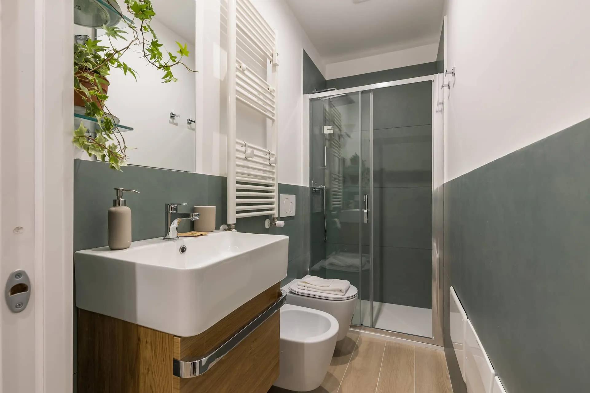 Bagno con mobile di legno, lavabo bianco, piastrelle verdi e doccia in vetro