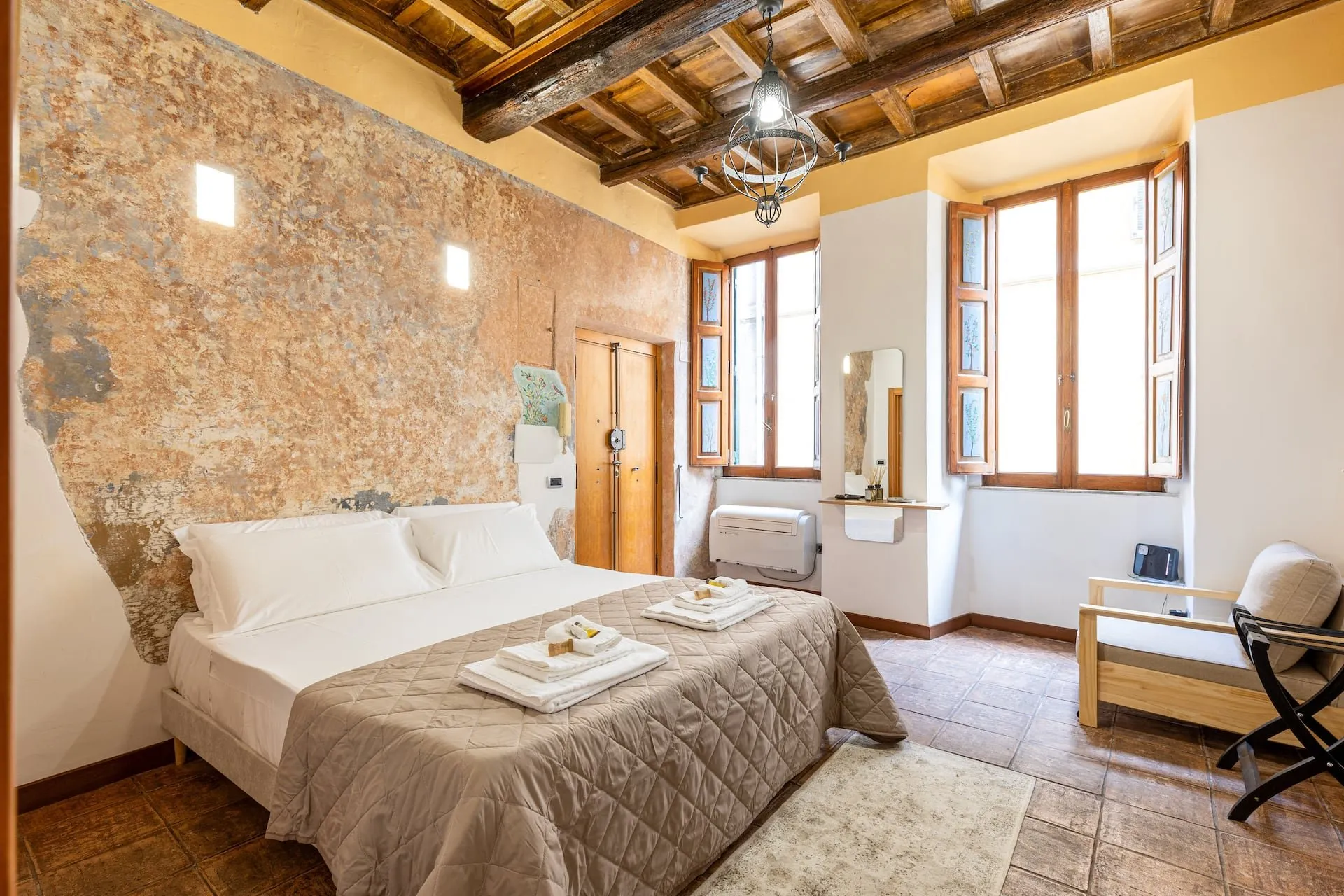 Camera con letto matrimoniale, muro di pietra antica e soffitto a travi, due finestre sul vicolo