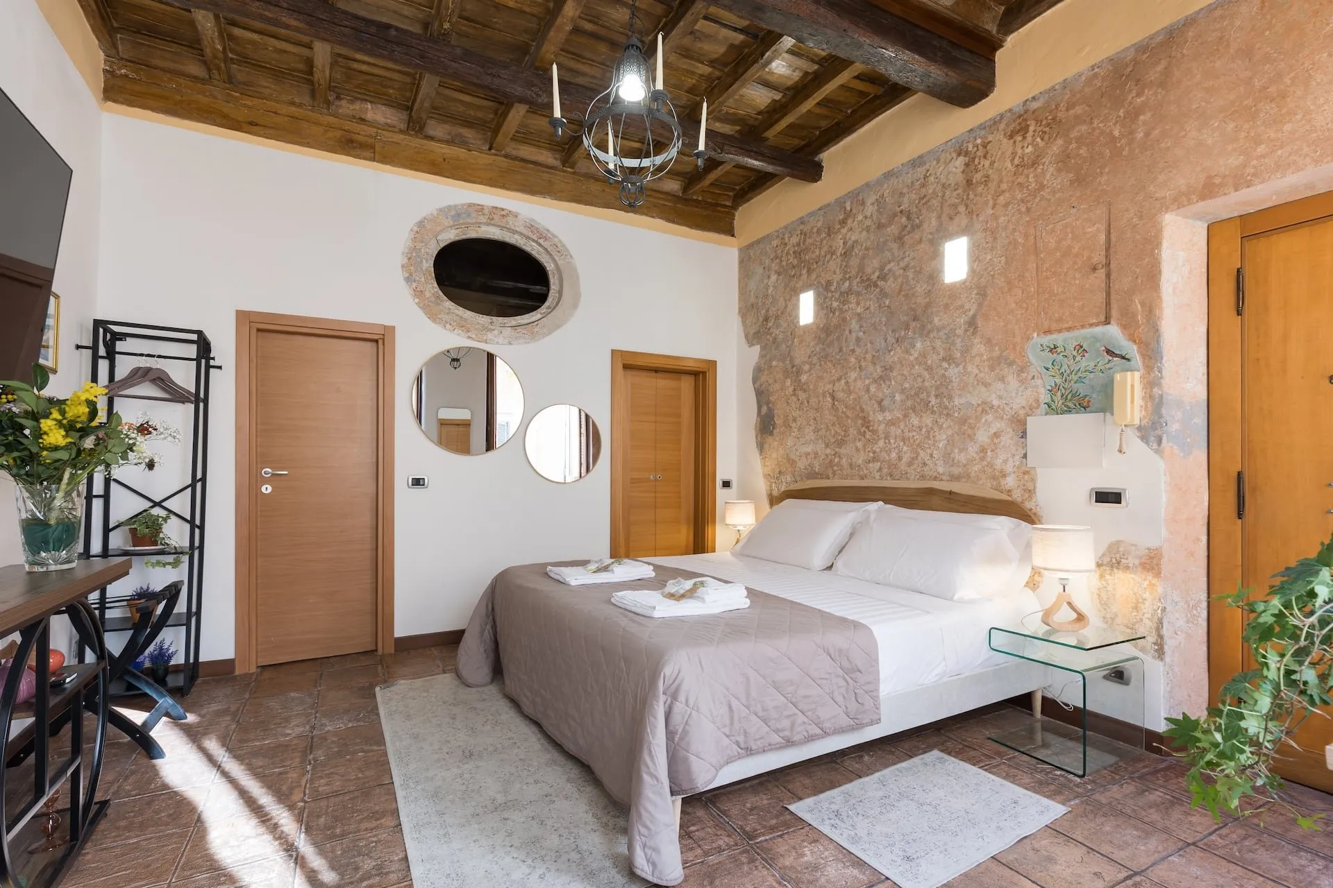 Camera vista dall'ingresso: letto matrimoniale, muro antico, porte di legno e piante in vaso