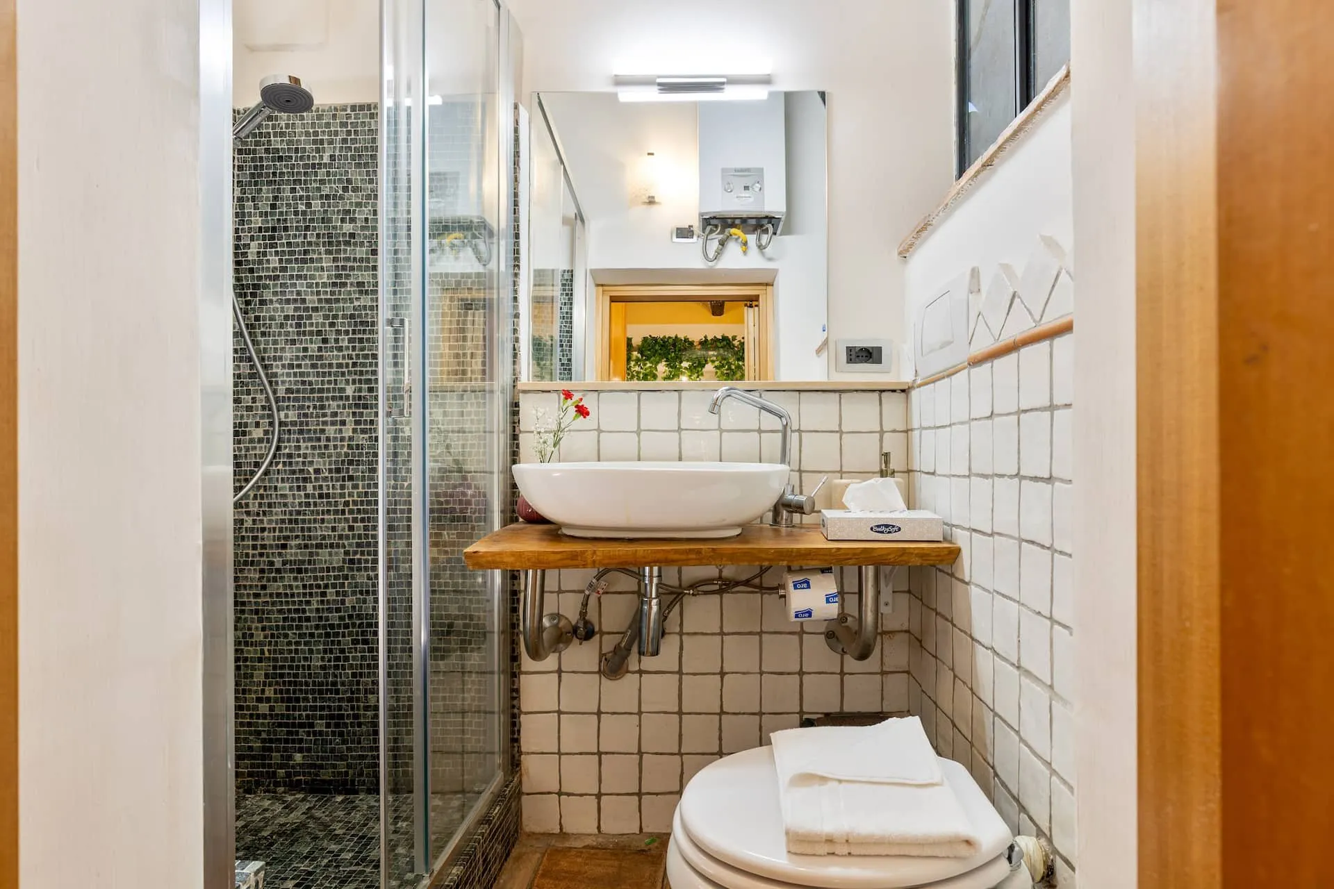 Bagno con lavabo d'appoggio su piano di legno, piastrelle bianche e doccia in mosaico