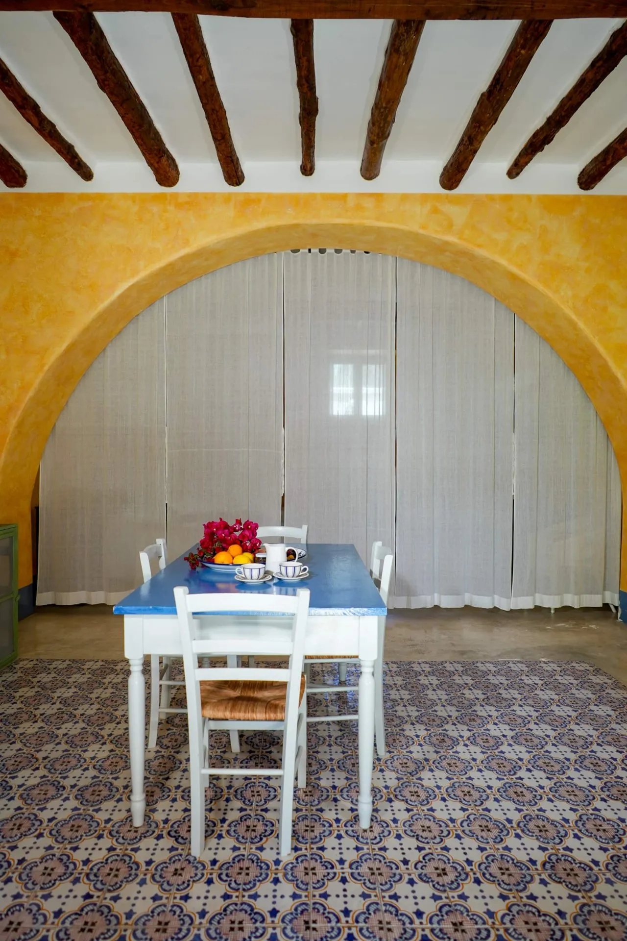 Tavolo bianco con tovaglia blu sotto un grande arco giallo, pavimento di maioliche