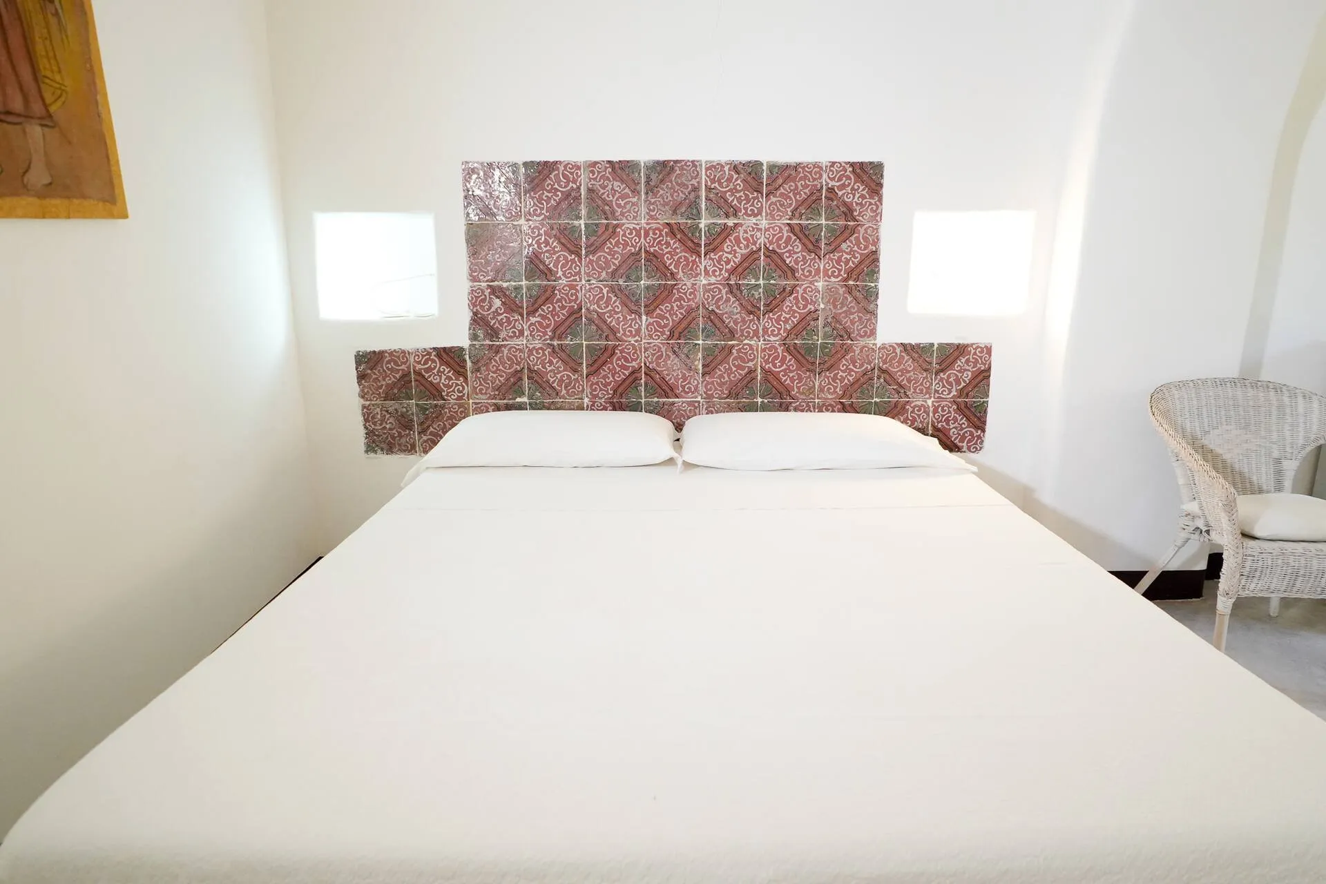 Letto matrimoniale con la testiera di piastrelle decorate, pareti bianche