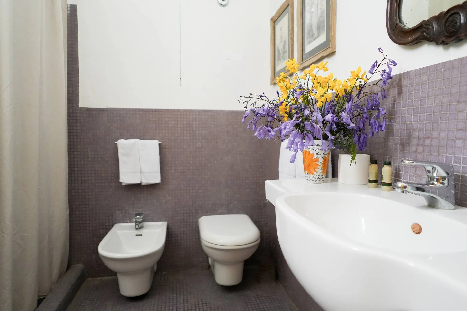 Bagno con vasca bianca, sanitari e fiori viola e gialli