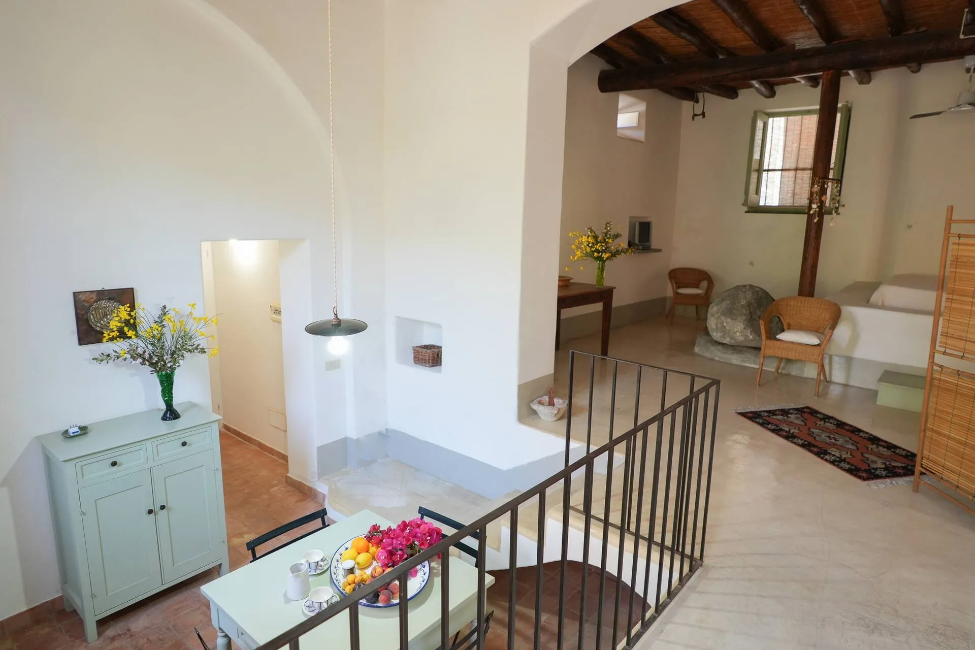 Soggiorno su due livelli con credenza verde chiaro, ringhiera e letto sul fondo