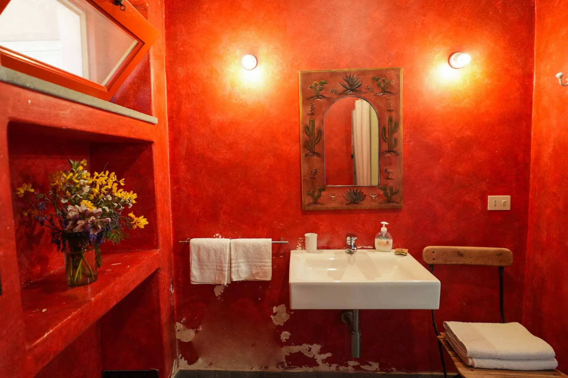 Bagno con pareti rosse, lavabo bianco, specchio decorato e fiori