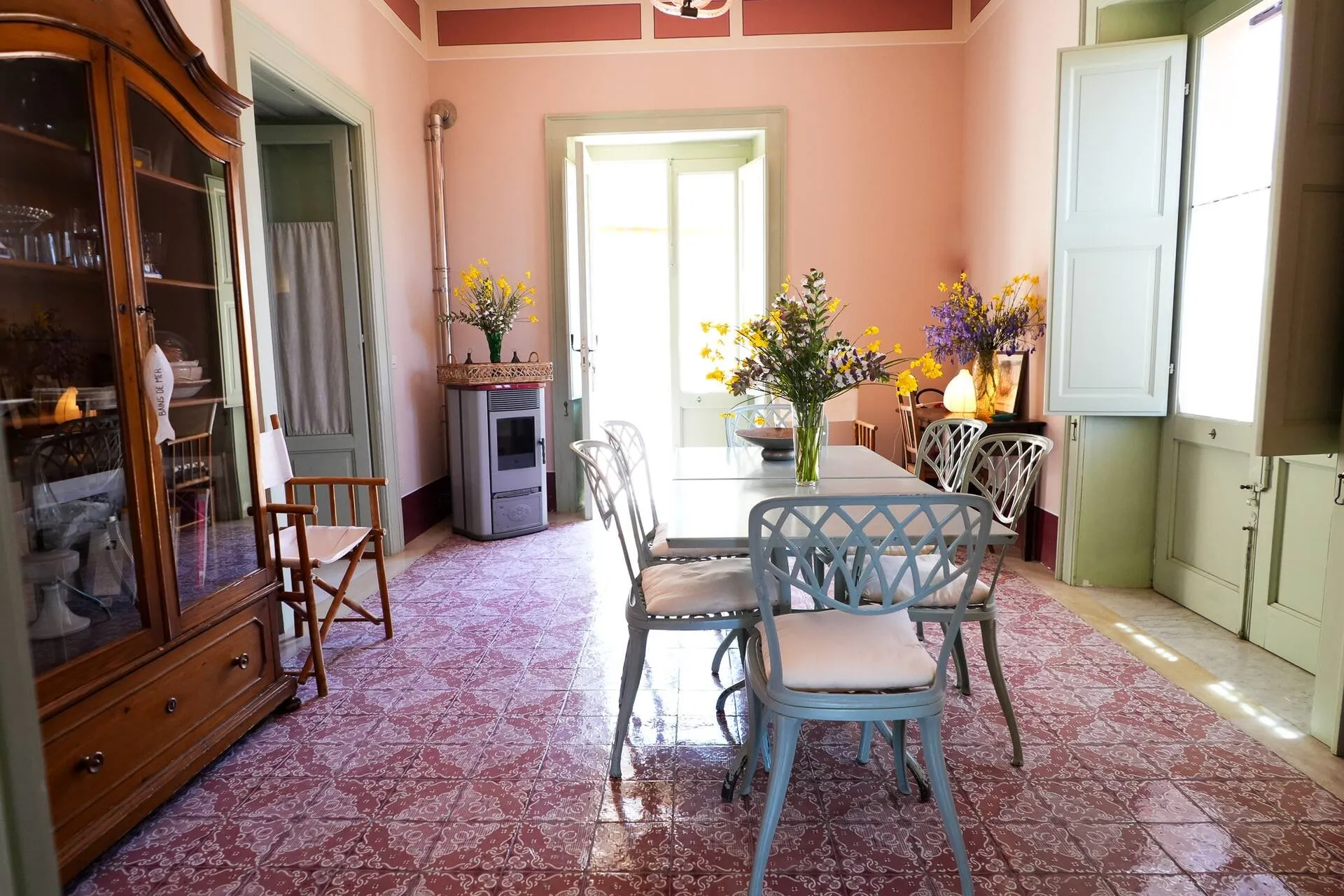 Sala da pranzo con pavimento di maioliche, tavolo bianco, credenza antica e porta finestra verde