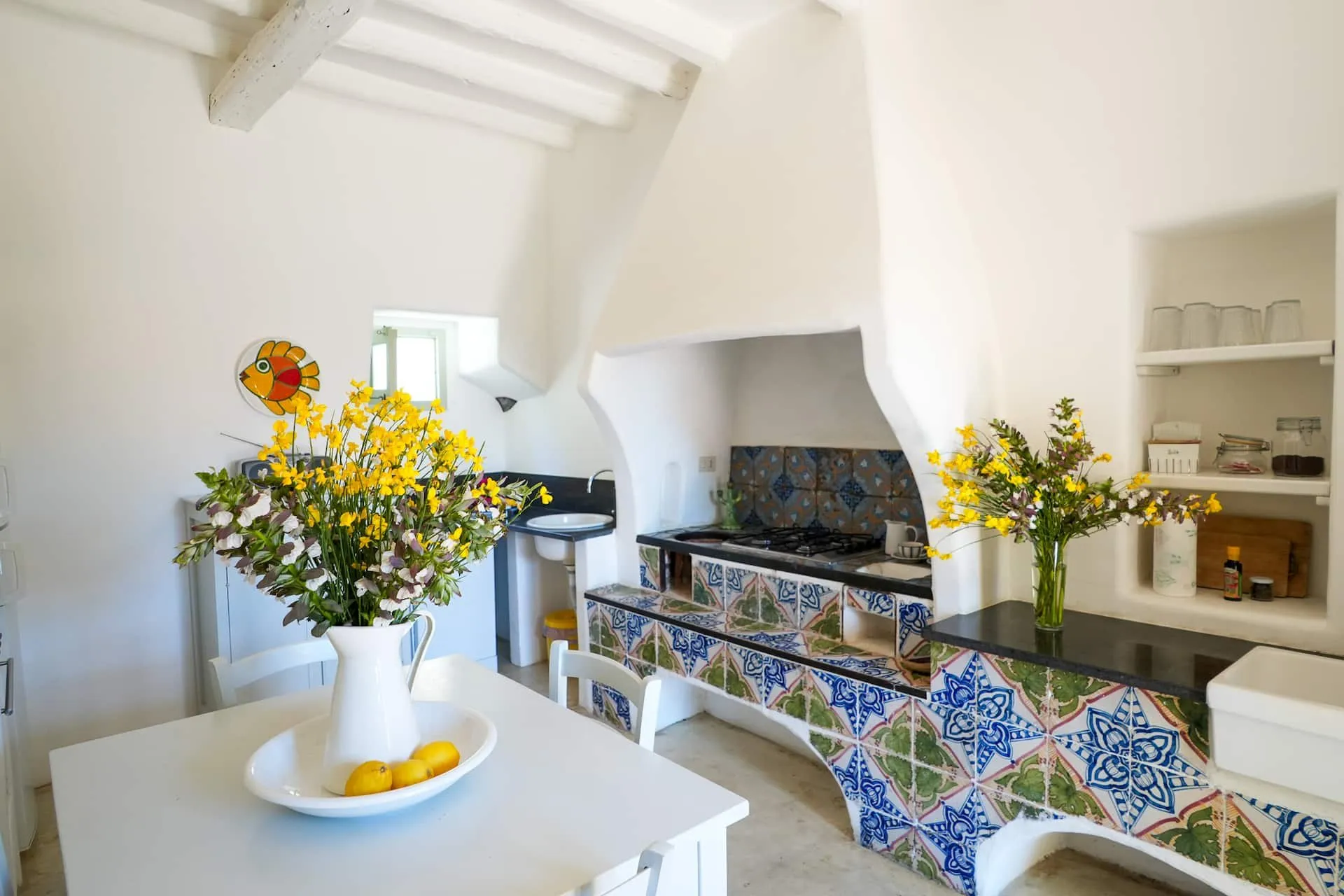 Cucina in muratura con piastrelle decorate e tavolo bianco con fiori