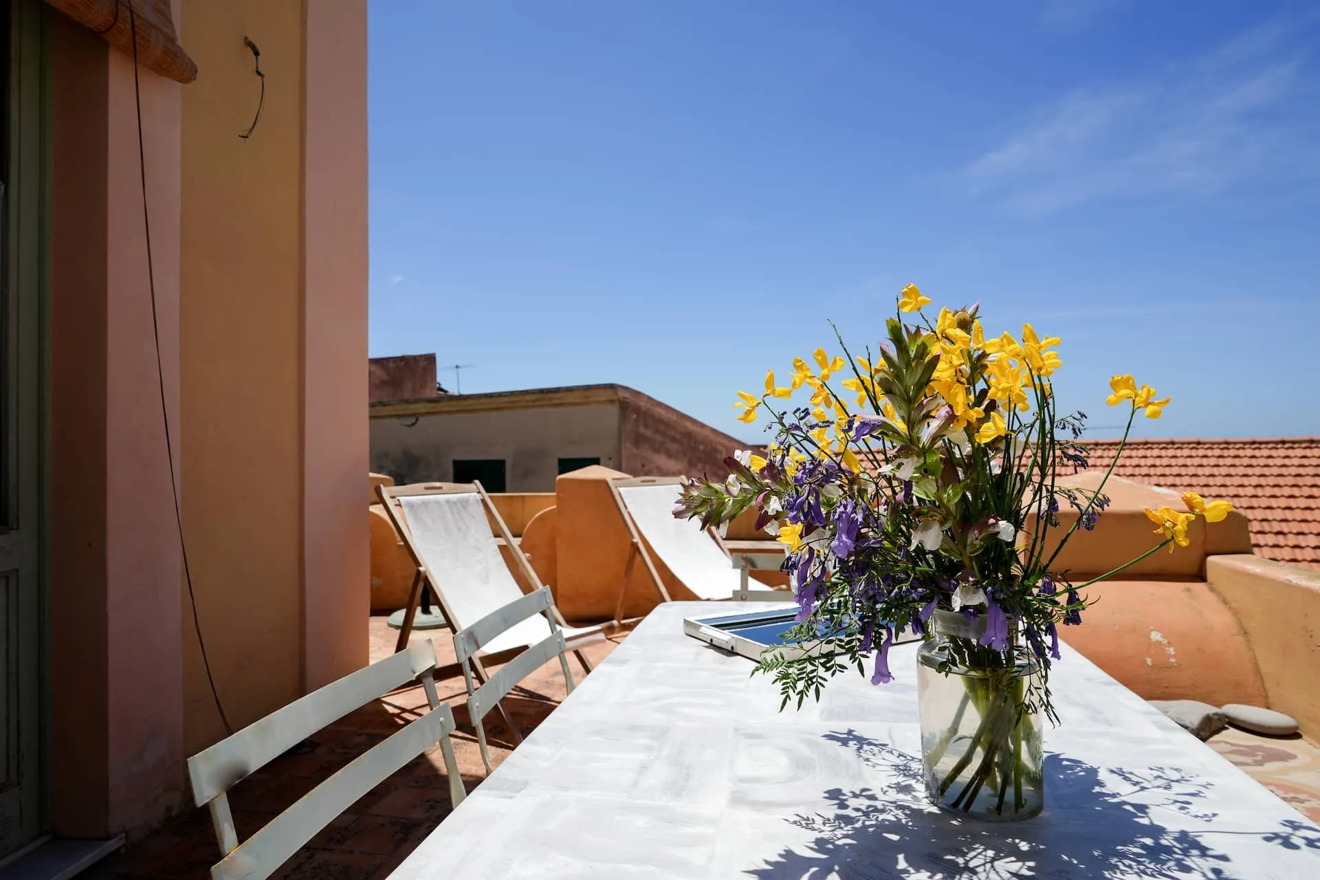 Tavola con fiori in terrazza, sdraio e tetti di coppi sotto il cielo