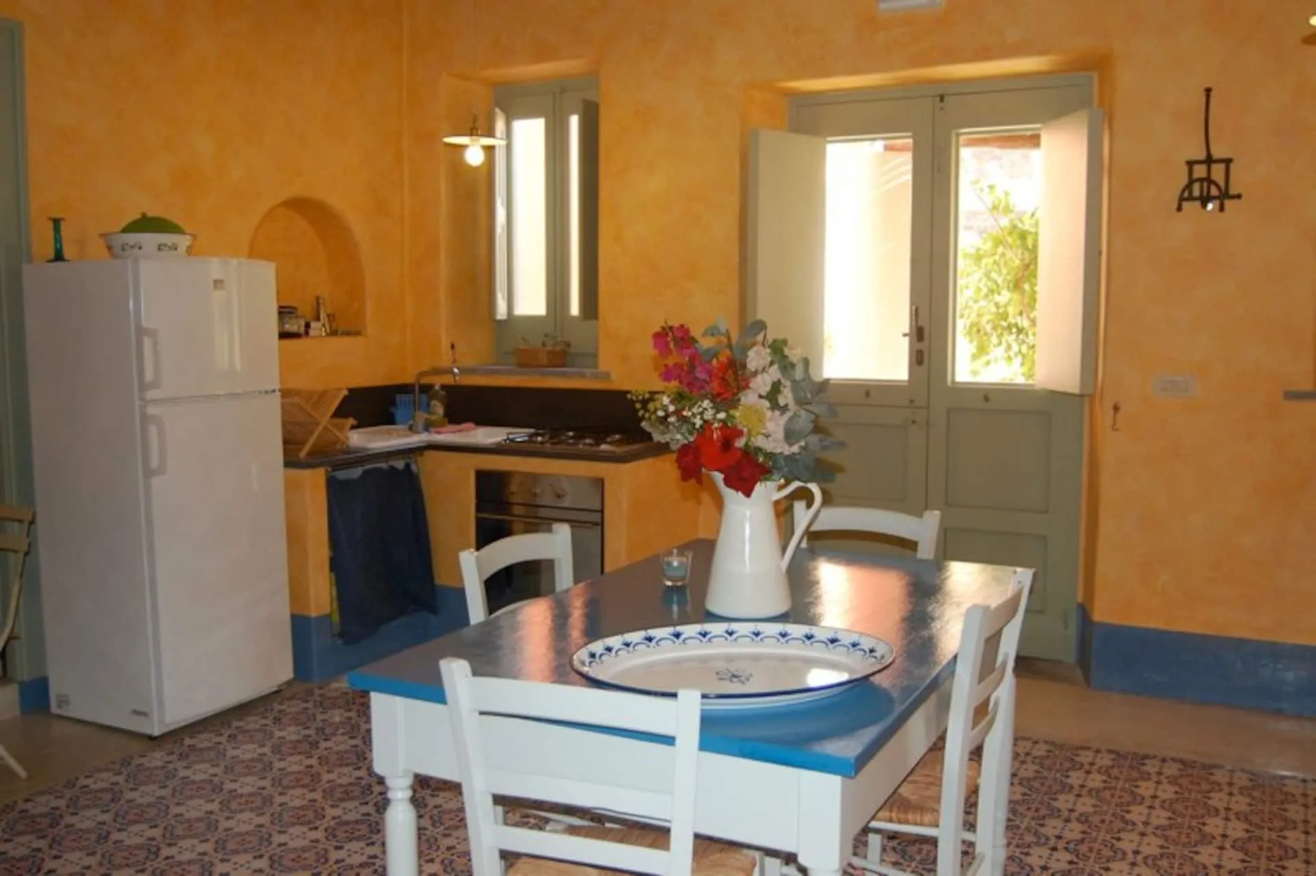 Cucina con pavimento di maioliche, tavolo bianco e porta finestra verde