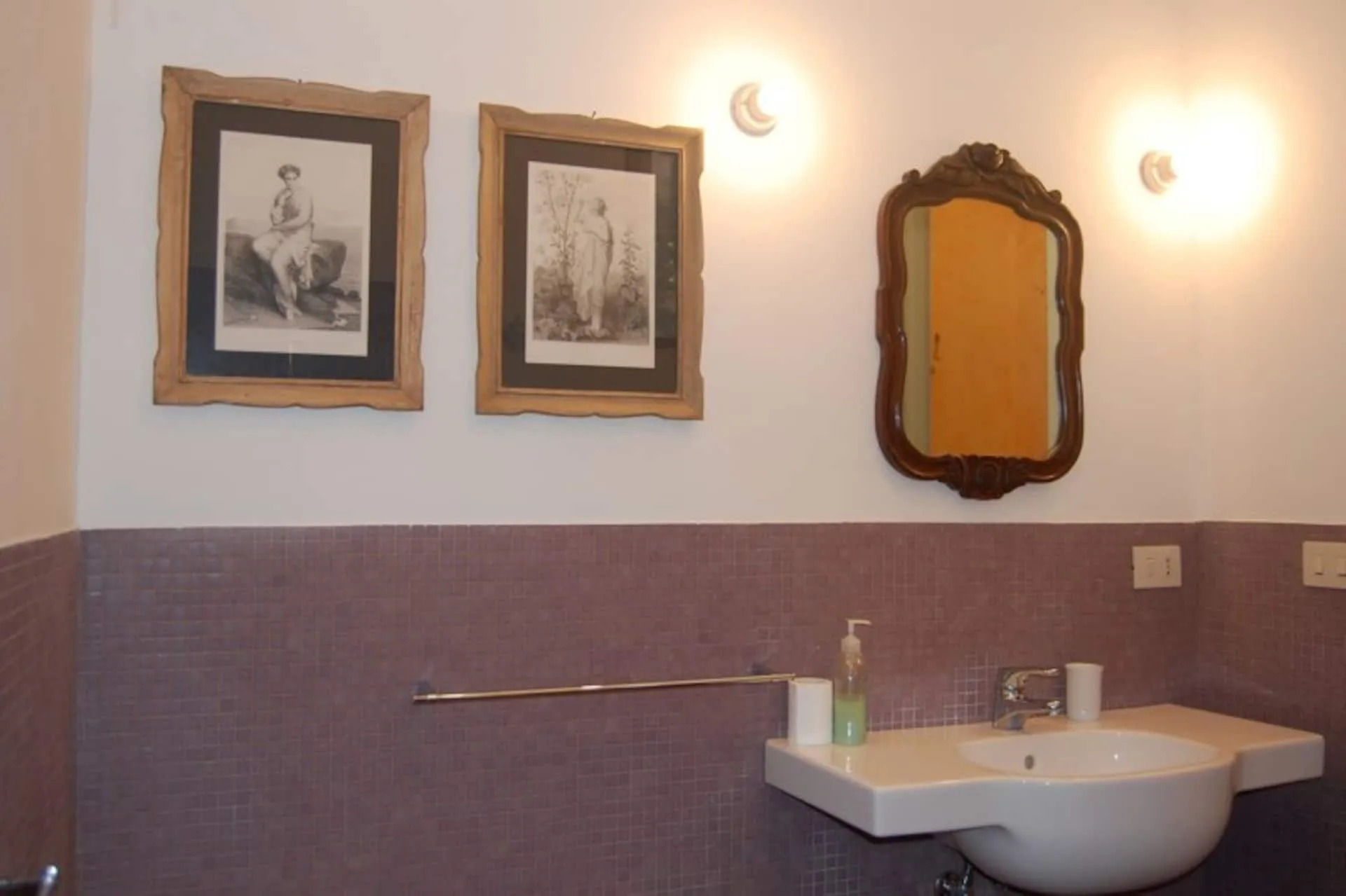 Bagno con stampe antiche, specchio in cornice di legno e lavabo bianco