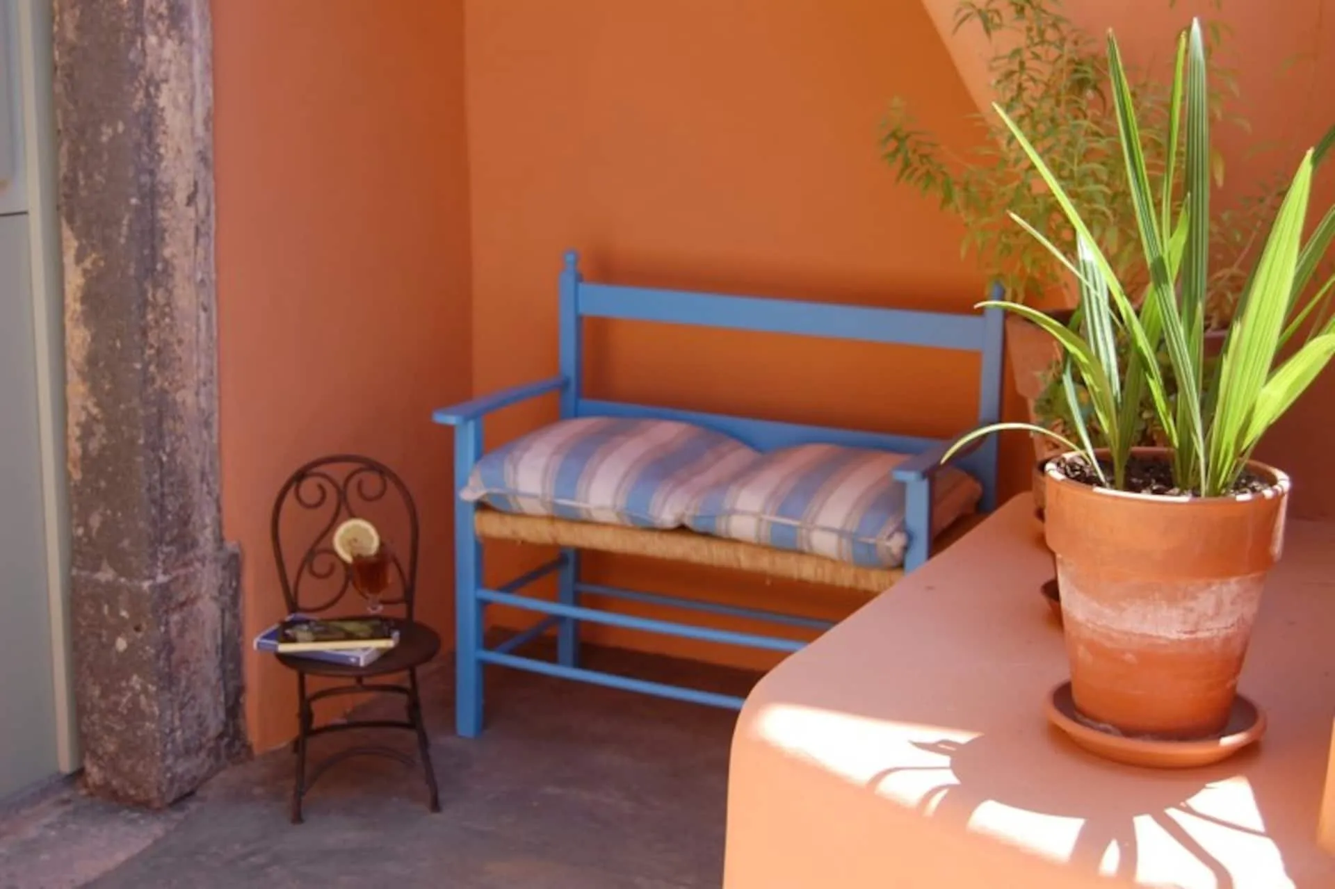 Panca azzurra con cuscini a righe su un muretto color terracotta, con una pianta in vaso