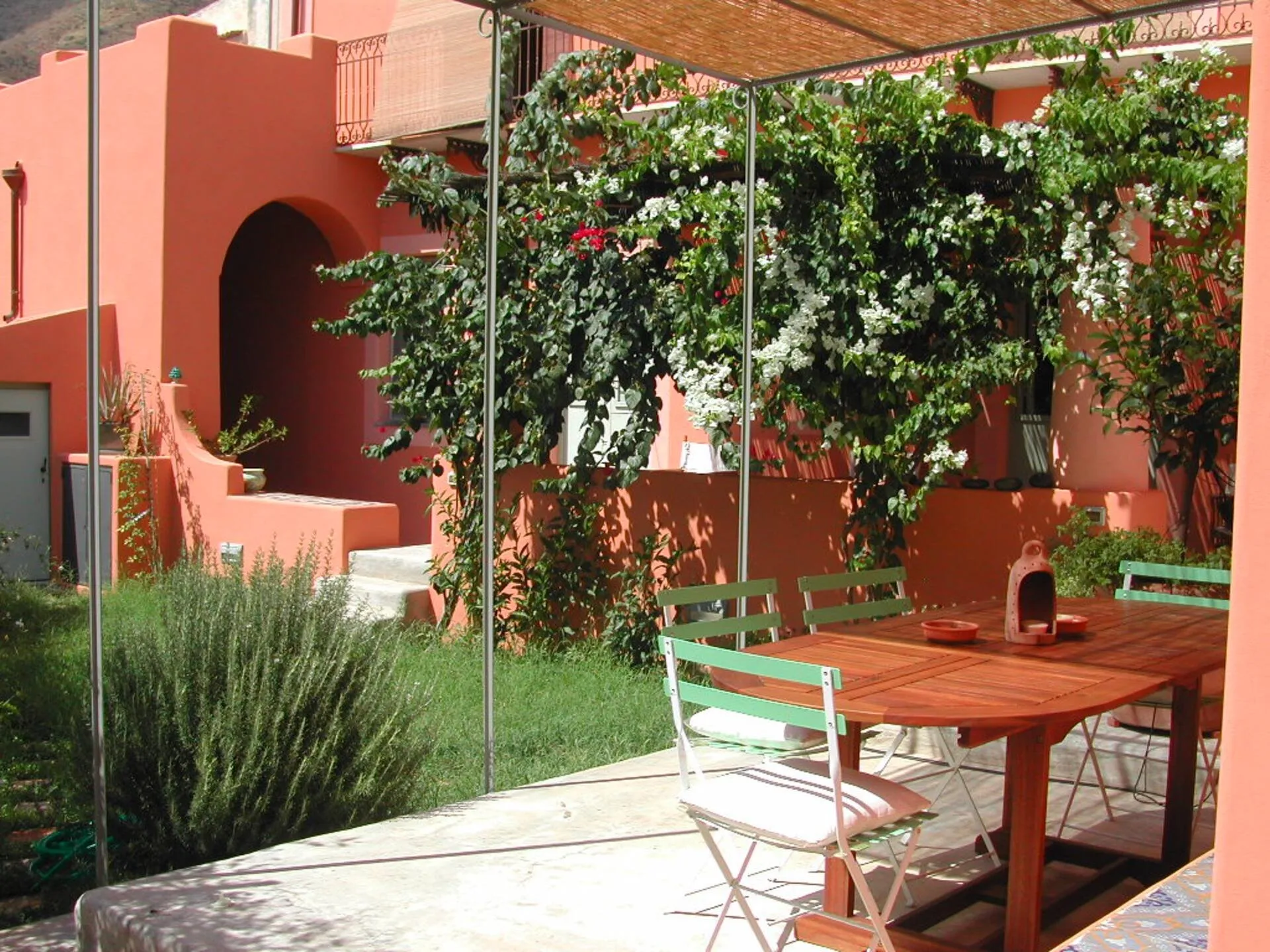 Giardino con pergolato, tavolo di legno e sedie verdi, fra bouganville e lavanda