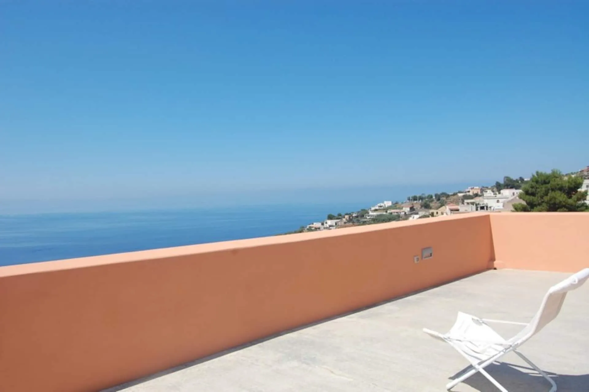Terrazza con la balaustra color terracotta e una sedia bianca, mare aperto all'orizzonte