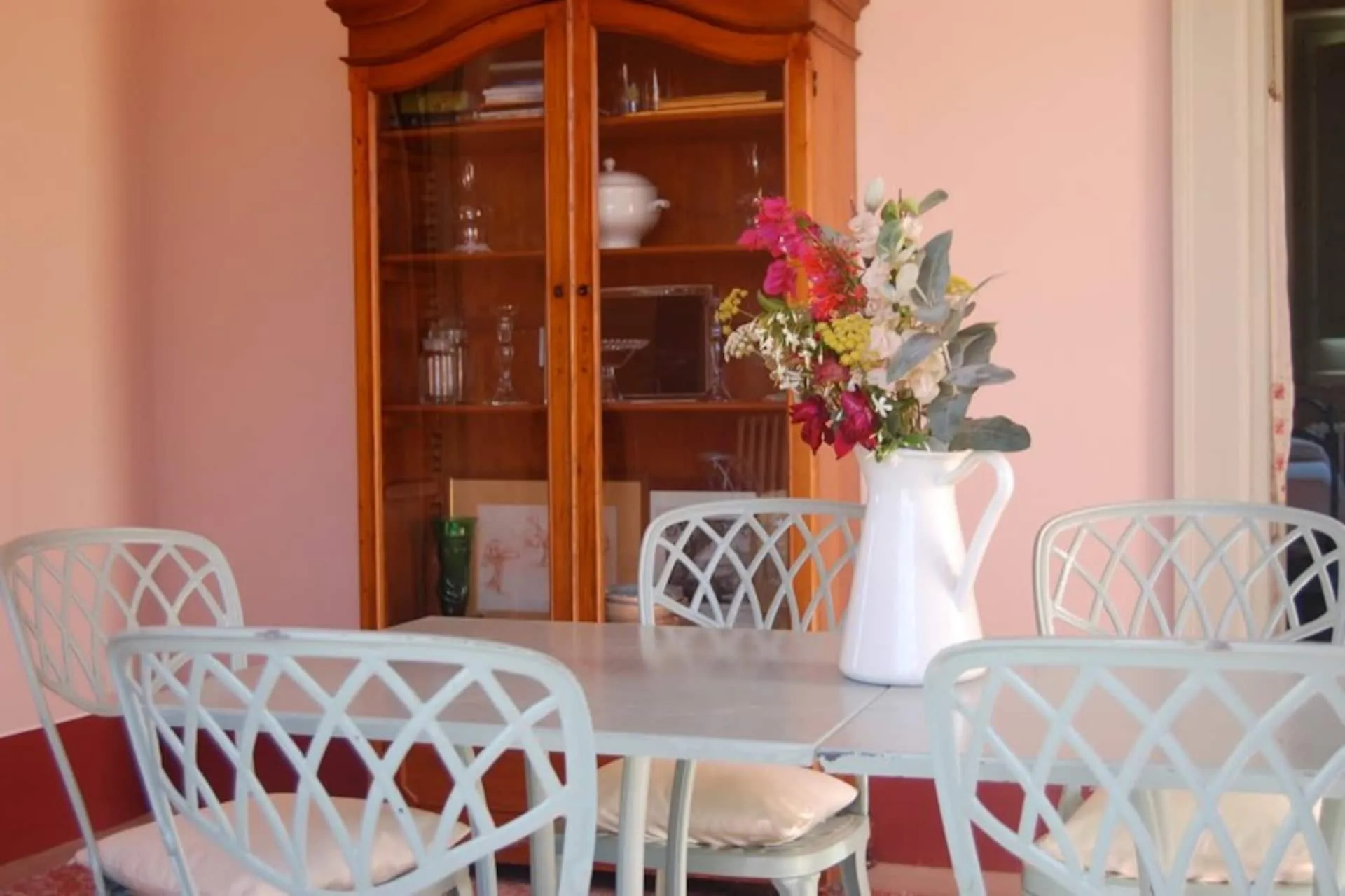 Sala da pranzo rosa con credenza di legno, tavolo bianco e sedie in ferro traforato
