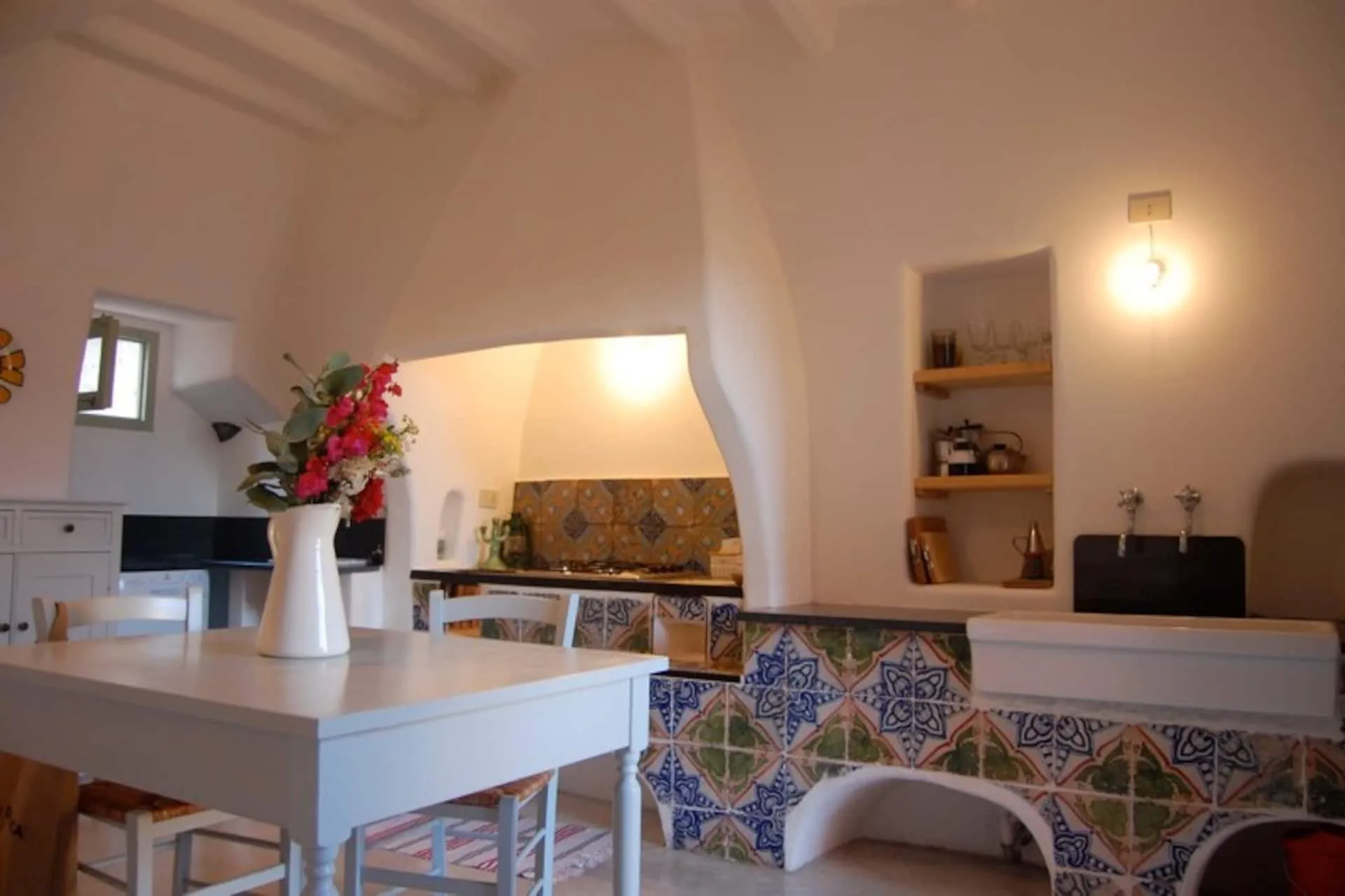 Cucina in muratura con piastrelle decorate blu e gialle, tavolo bianco e fiori rossi