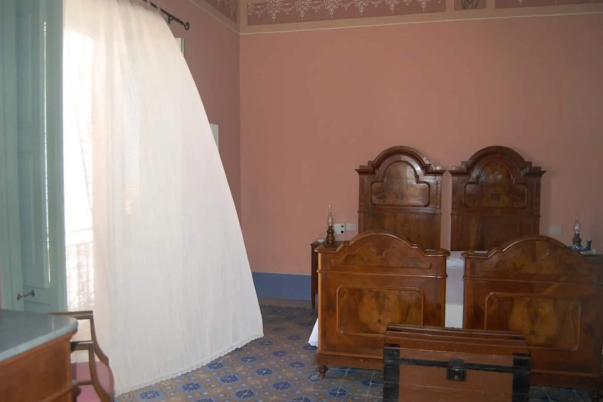 Camera con letti antichi in legno intarsiato e una tenda bianca mossa dal vento