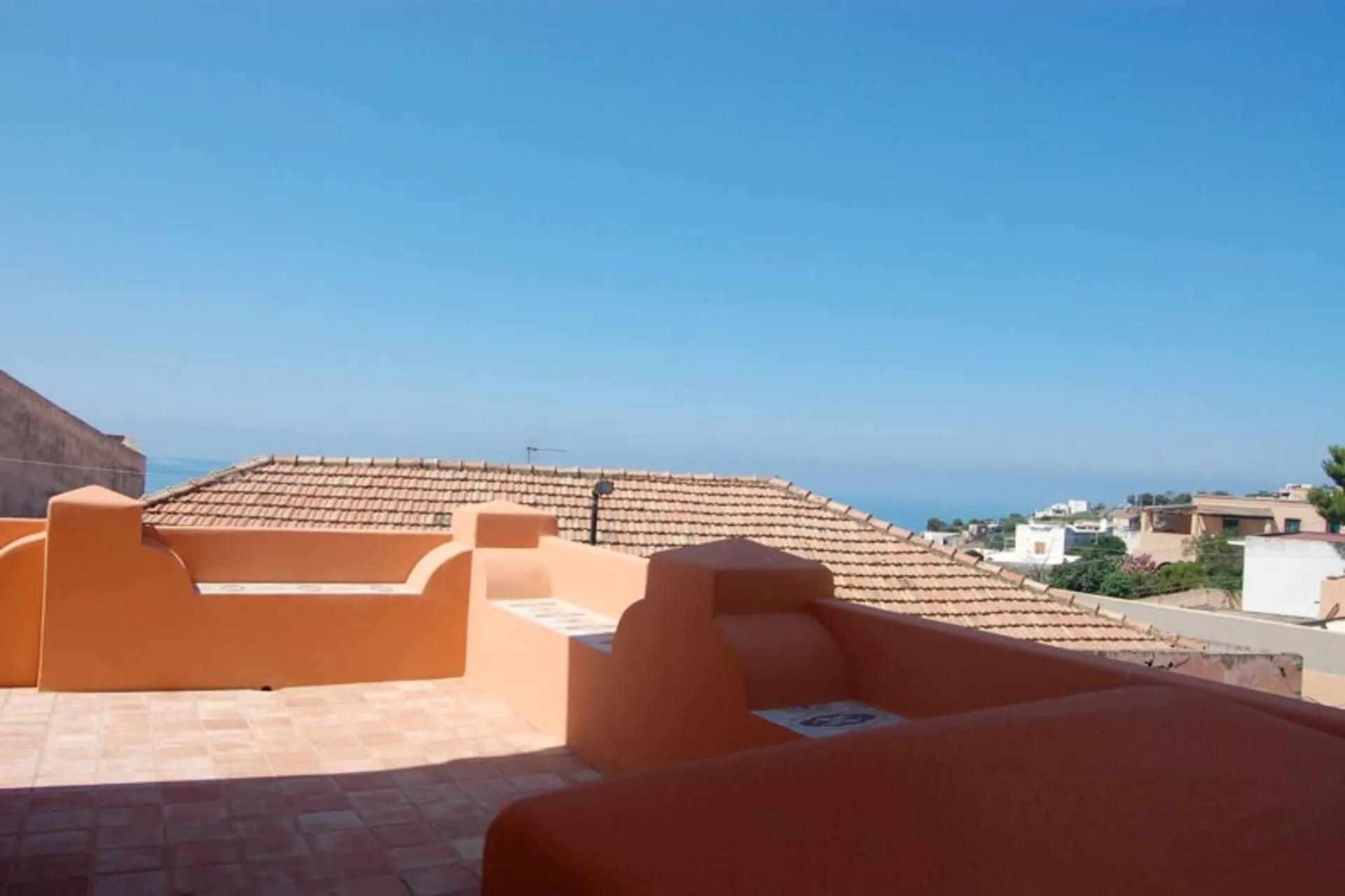 Terrazza sul tetto con muretti color terracotta, case e mare sullo sfondo