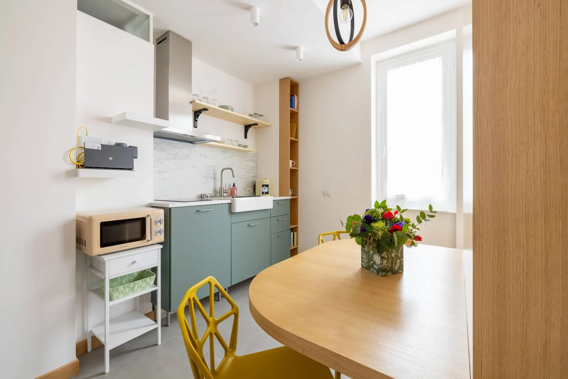Cucina verde salvia con tavolo di legno a mezzaluna e sedie gialle