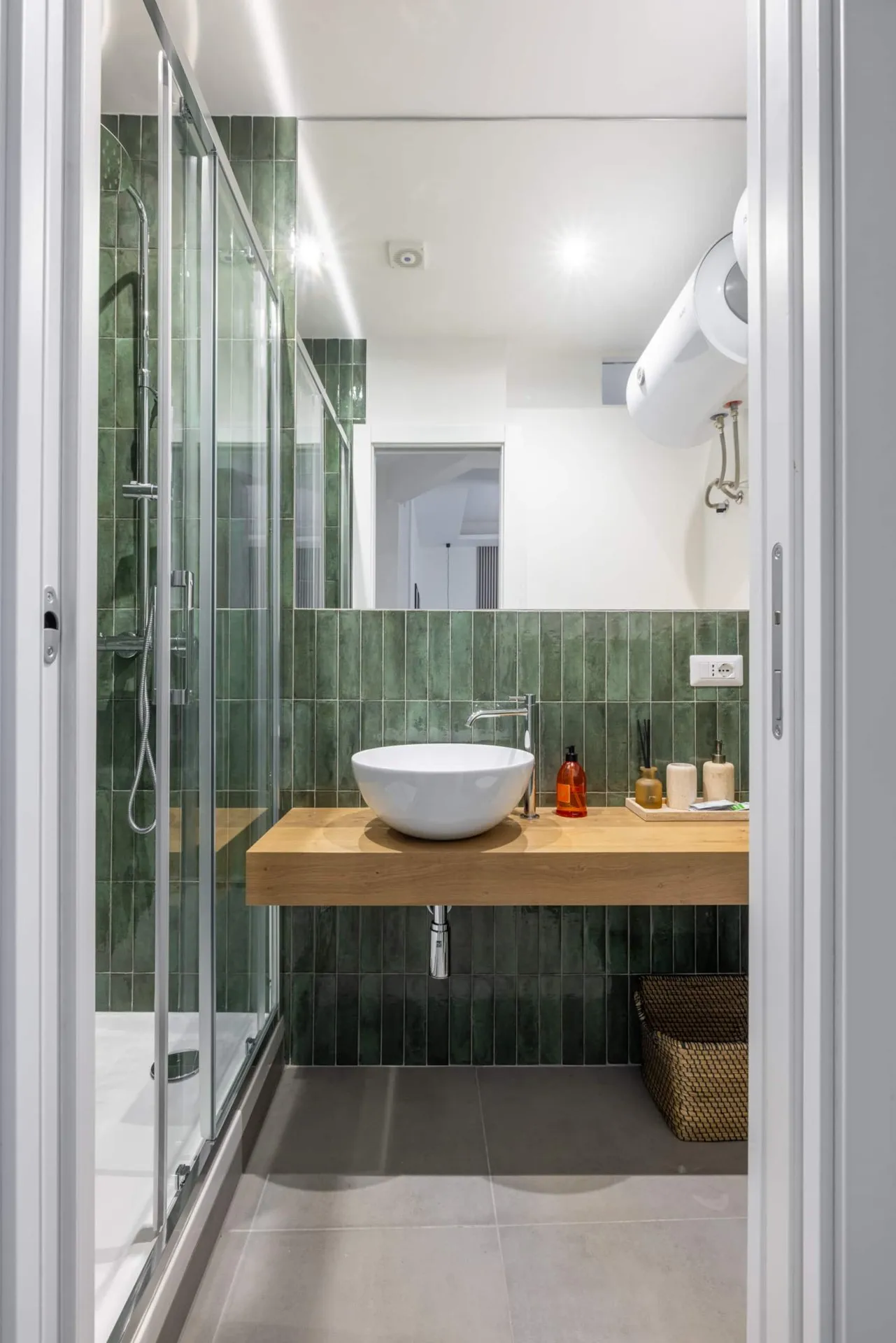 Bagno con piastrelle verdi, lavabo su piano di legno e doccia in vetro
