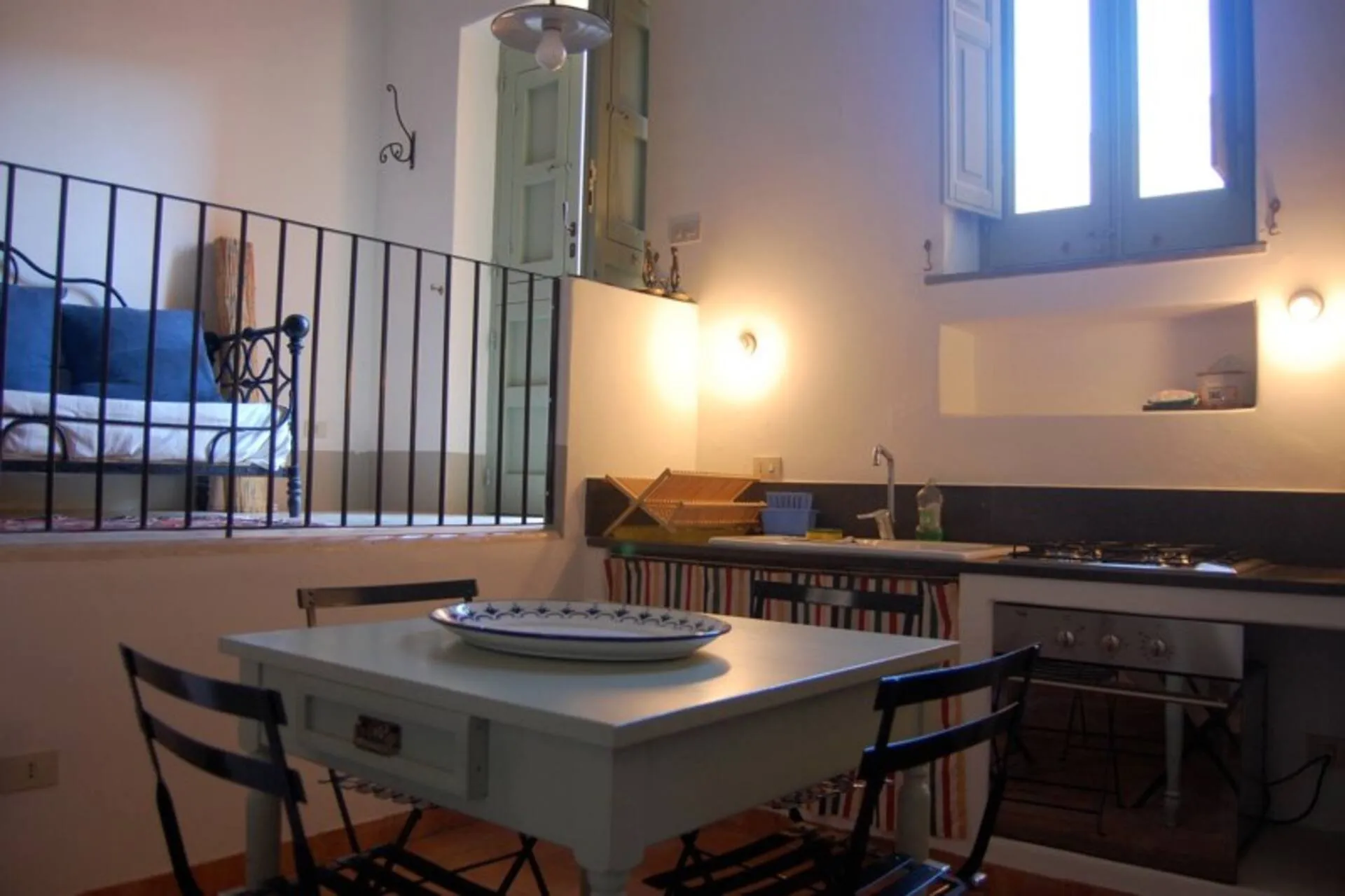 Zona pranzo con tavolo verde chiaro e sedie di ferro, angolo cottura e ringhiera