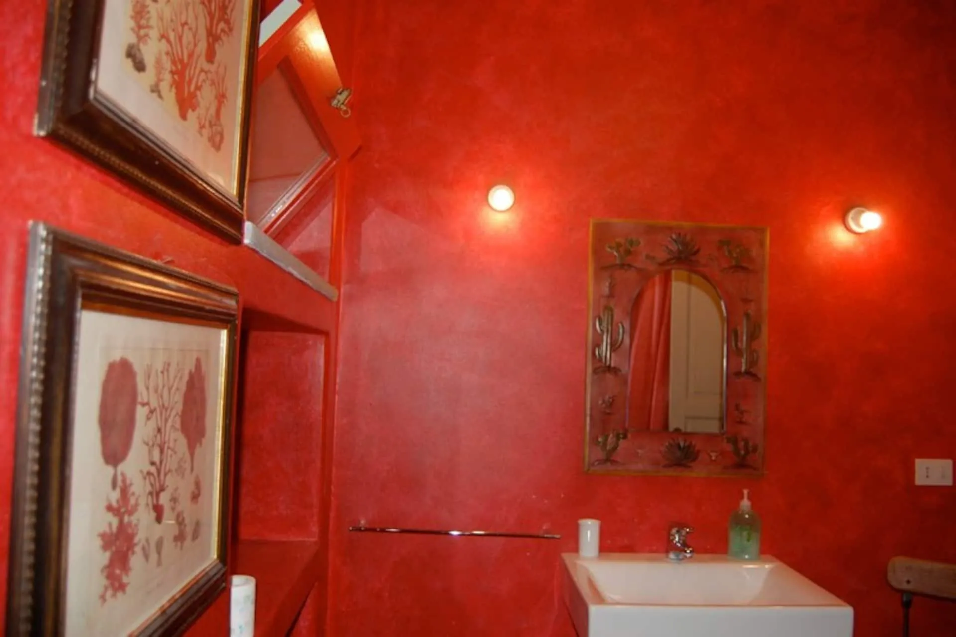 Bagno con pareti rosse, specchio decorato e stampe incorniciate