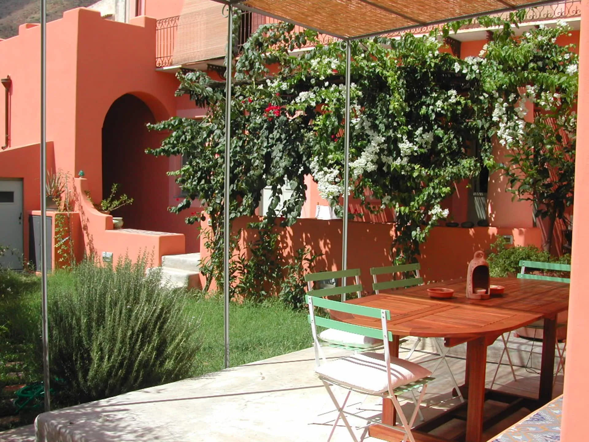 Giardino con pergolato, tavolo di legno e sedie verdi, fra bouganville e lavanda