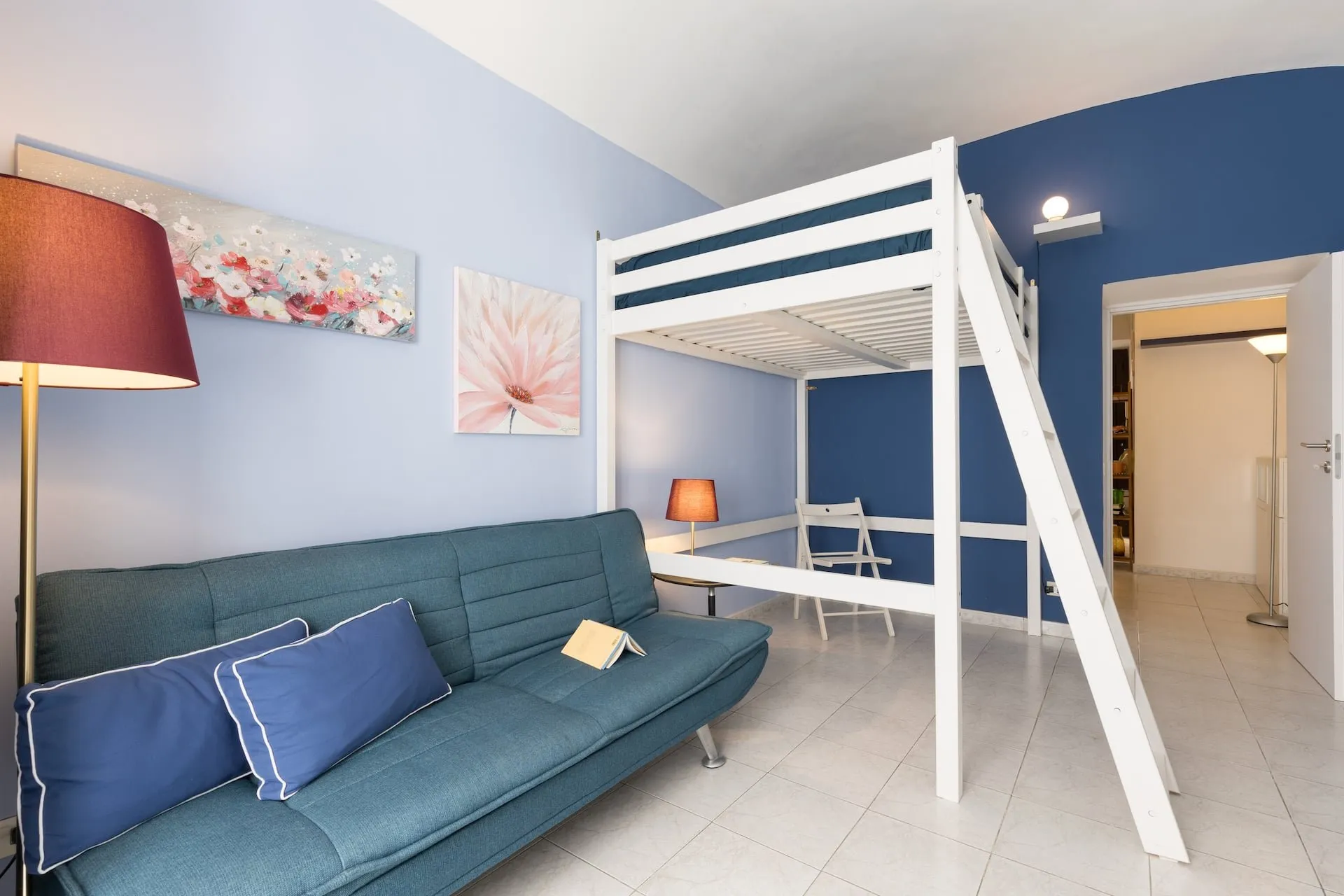 Monolocale con pareti azzurre, divano blu e letto a soppalco bianco
