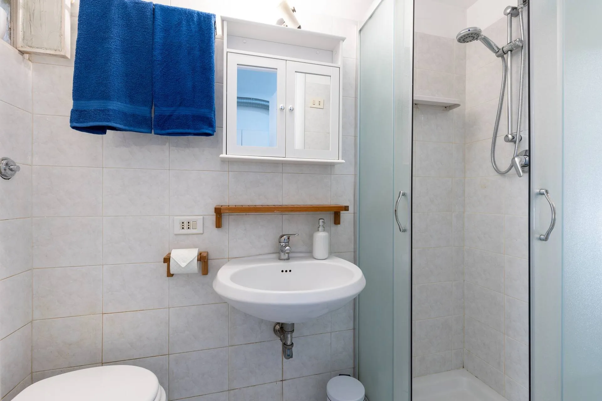 Bagno bianco con lavabo, doccia e asciugamano blu