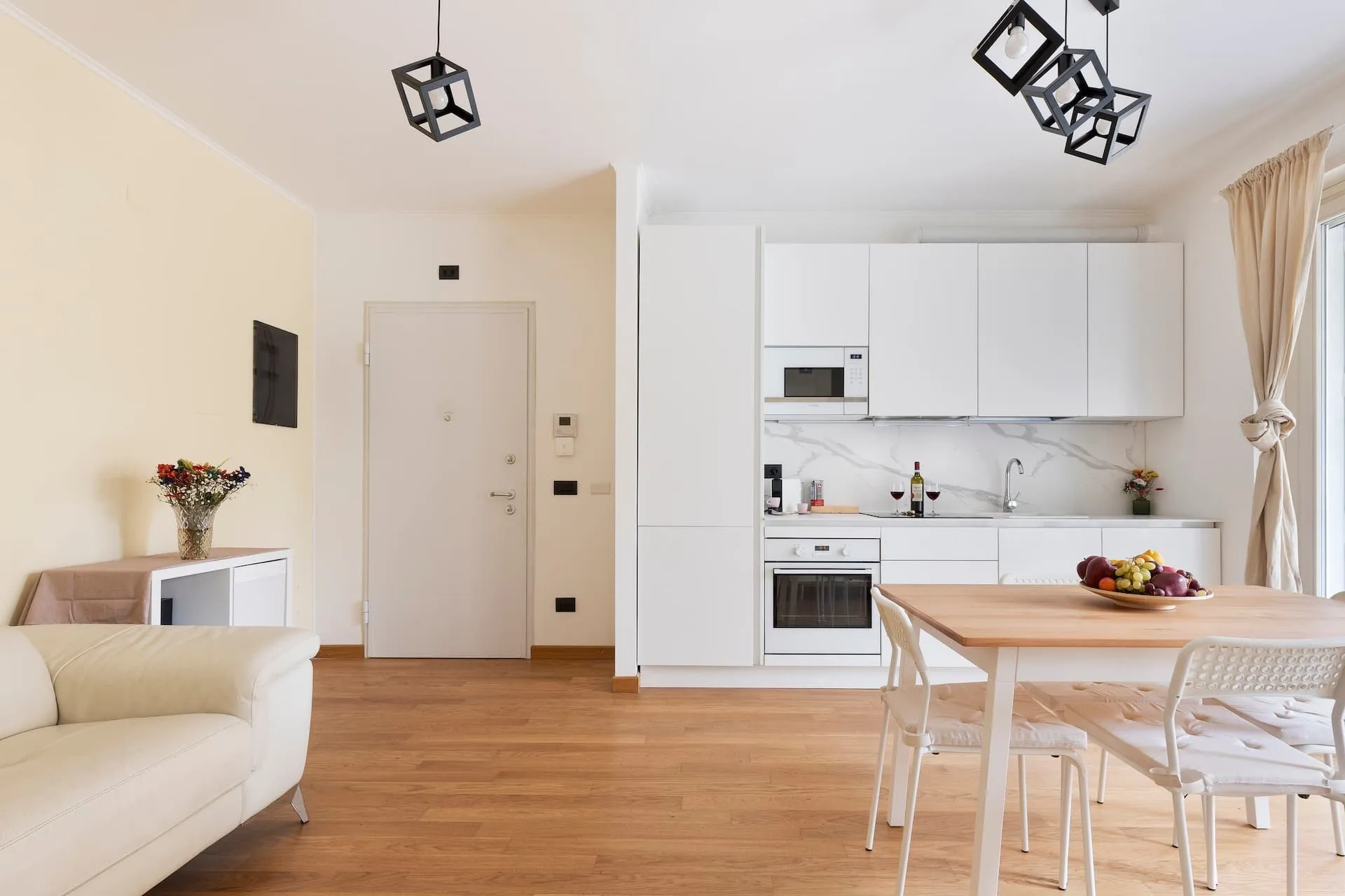 Soggiorno con parquet, cucina bianca a vista e tavolo di legno, divano bianco in primo piano