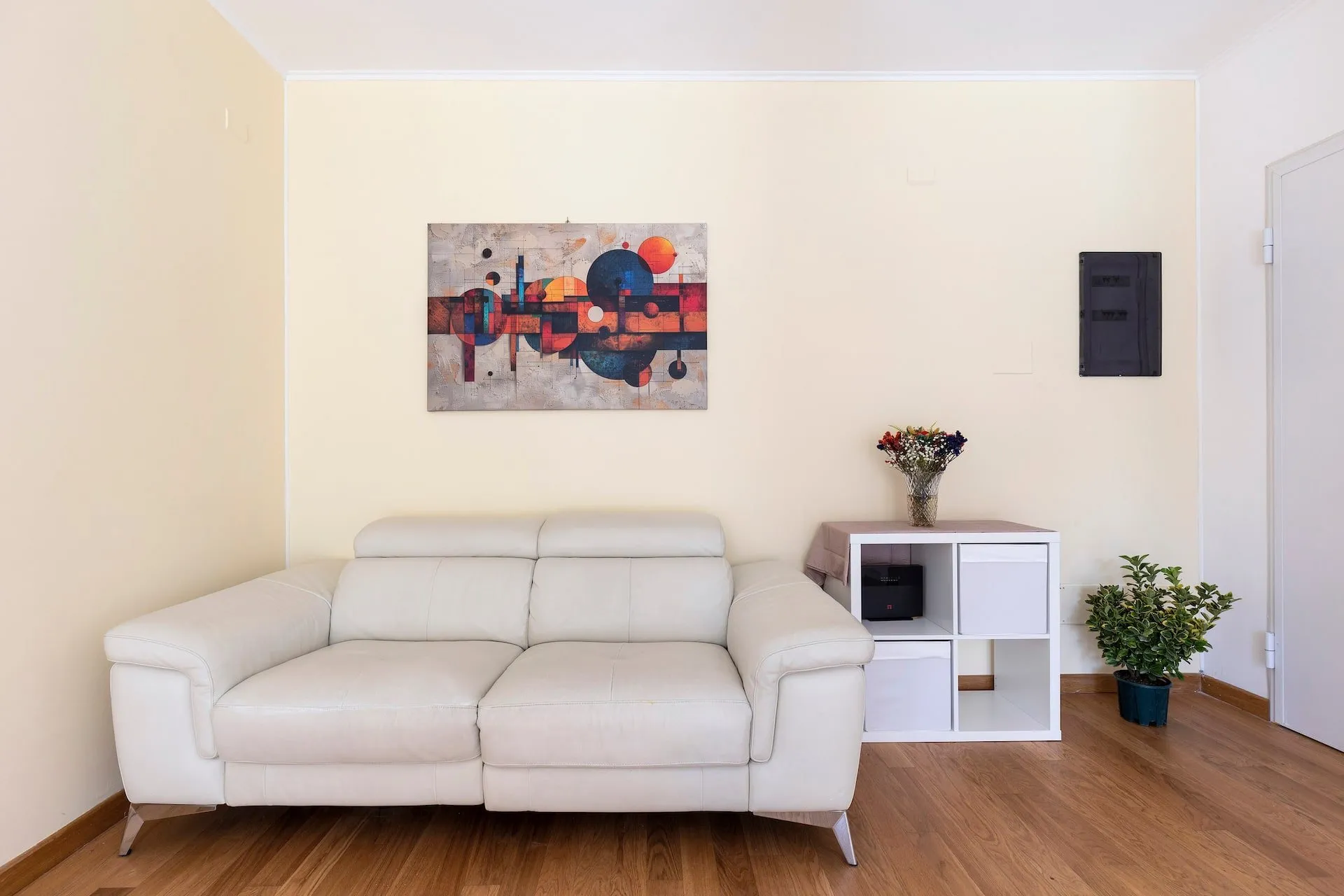 Divano bianco in pelle, quadro astratto e mobiletto bianco