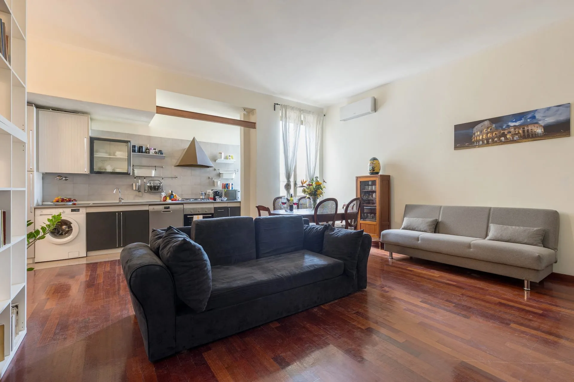 Soggiorno ampio con parquet scuro, due divani e cucina a vista sul fondo
