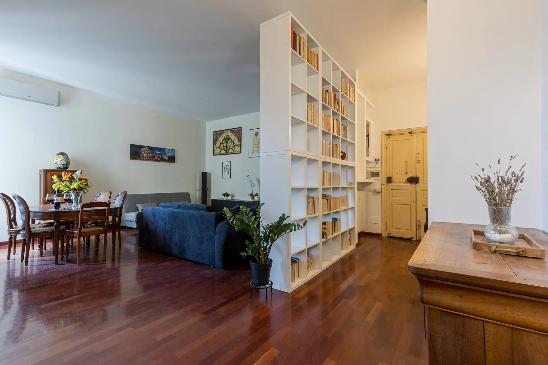 Soggiorno visto dall'ingresso: libreria bianca a tutta altezza, divano blu e tavolo da pranzo