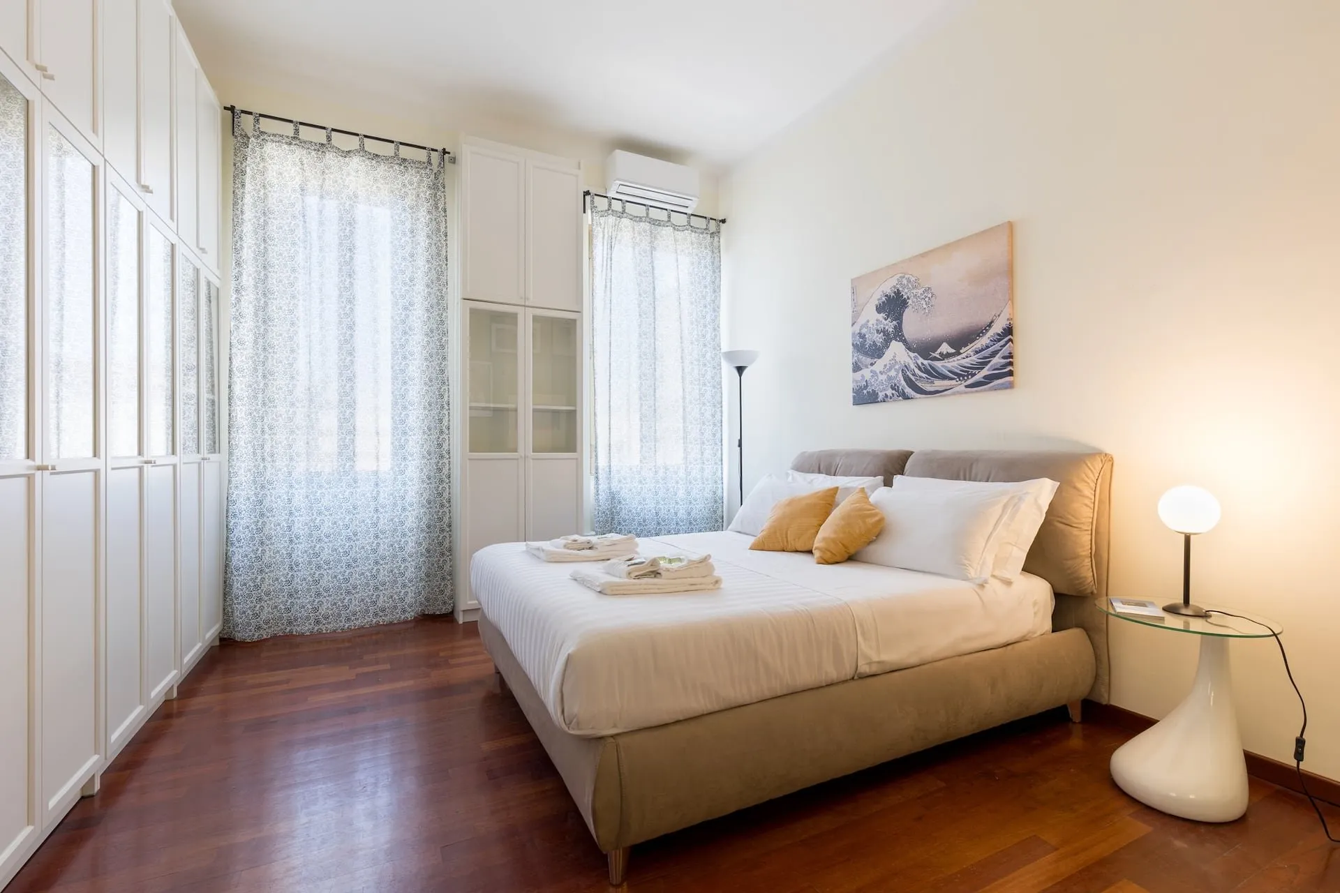 Camera con letto matrimoniale, armadio bianco a tutta parete e due finestre con tende chiare