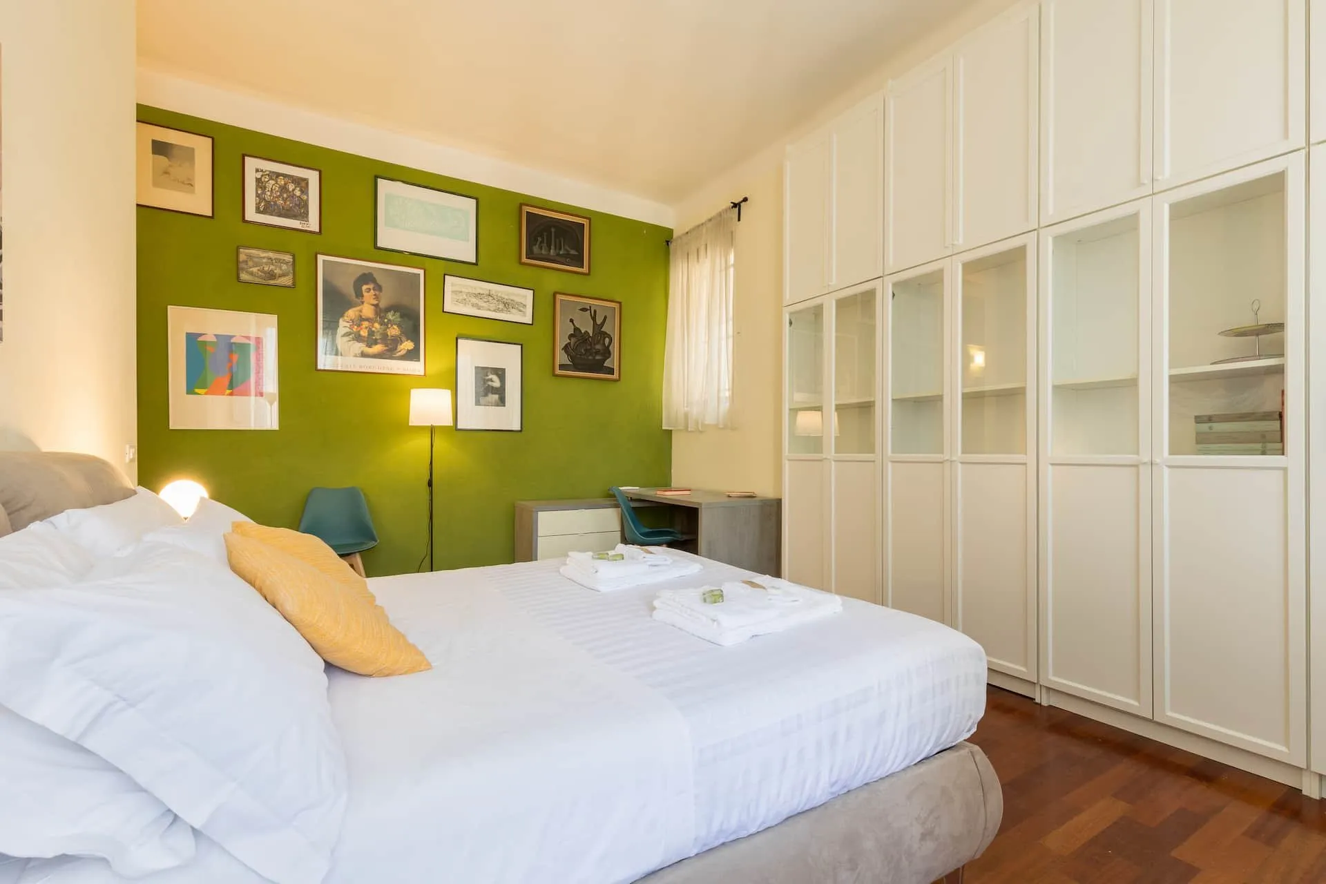 Seconda camera con parete verde e quadri, letto matrimoniale e armadio bianco